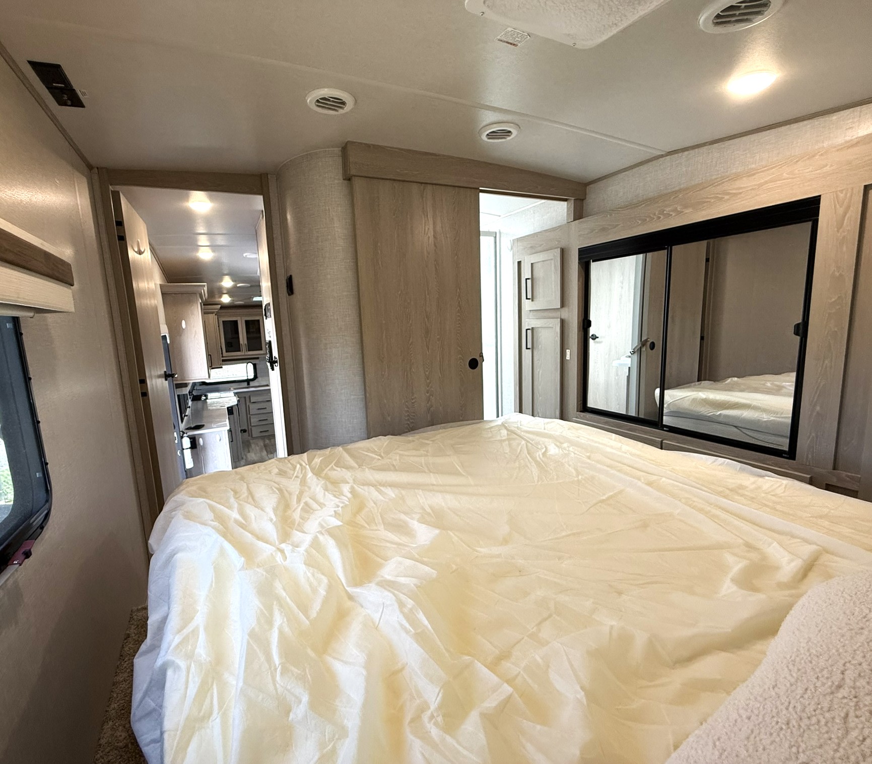 Explore this RV rental's cozy bedroom: a large bed, mirrored closet, and open view to the kitchen area.. Forest River Rockwood Ultra Lite 2023