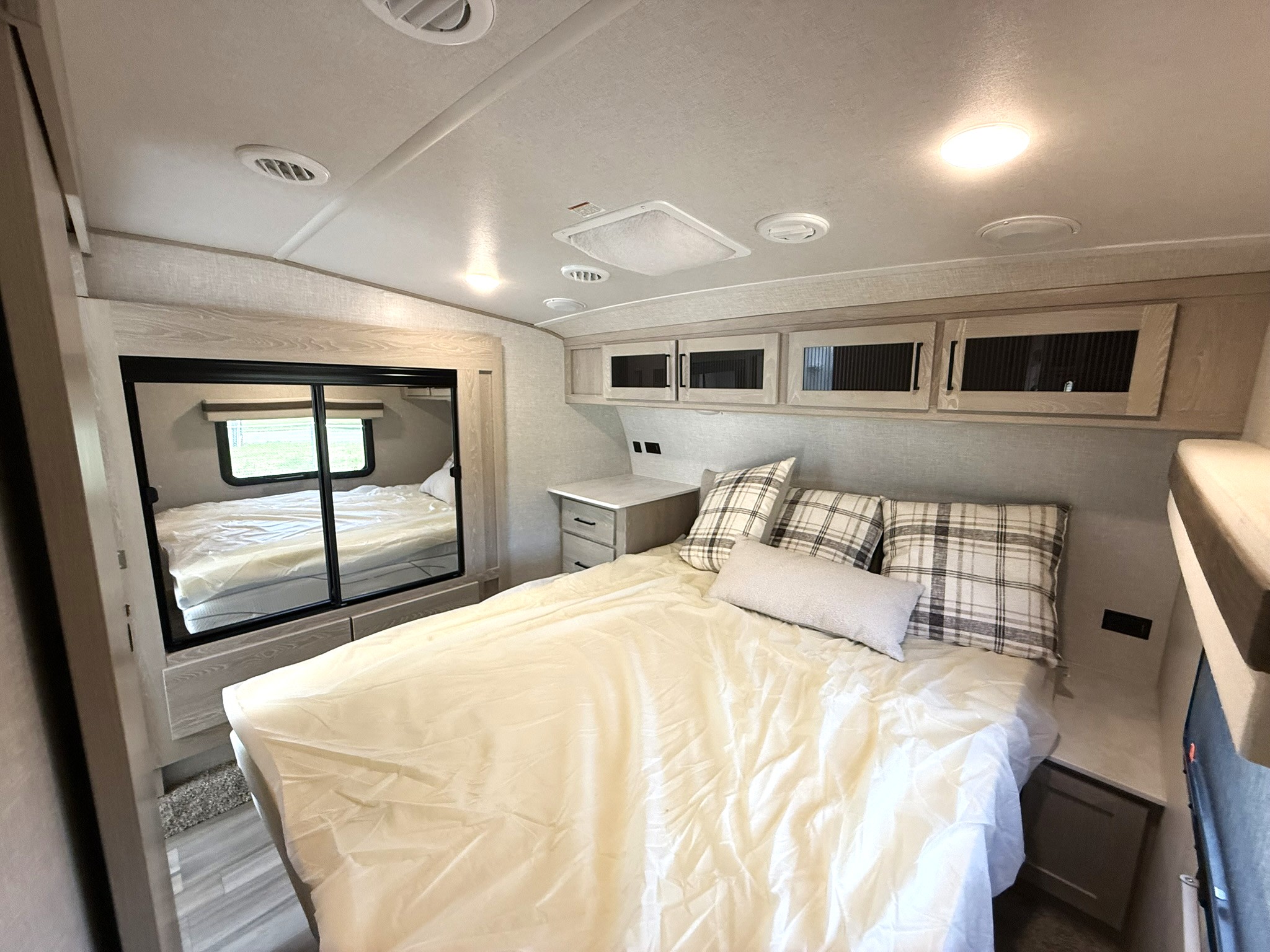 Explore this inviting RV rental bedroom with a comfy bed, plaid pillows, overhead storage, and bright ceiling lights.. Forest River Rockwood Ultra Lite 2023
