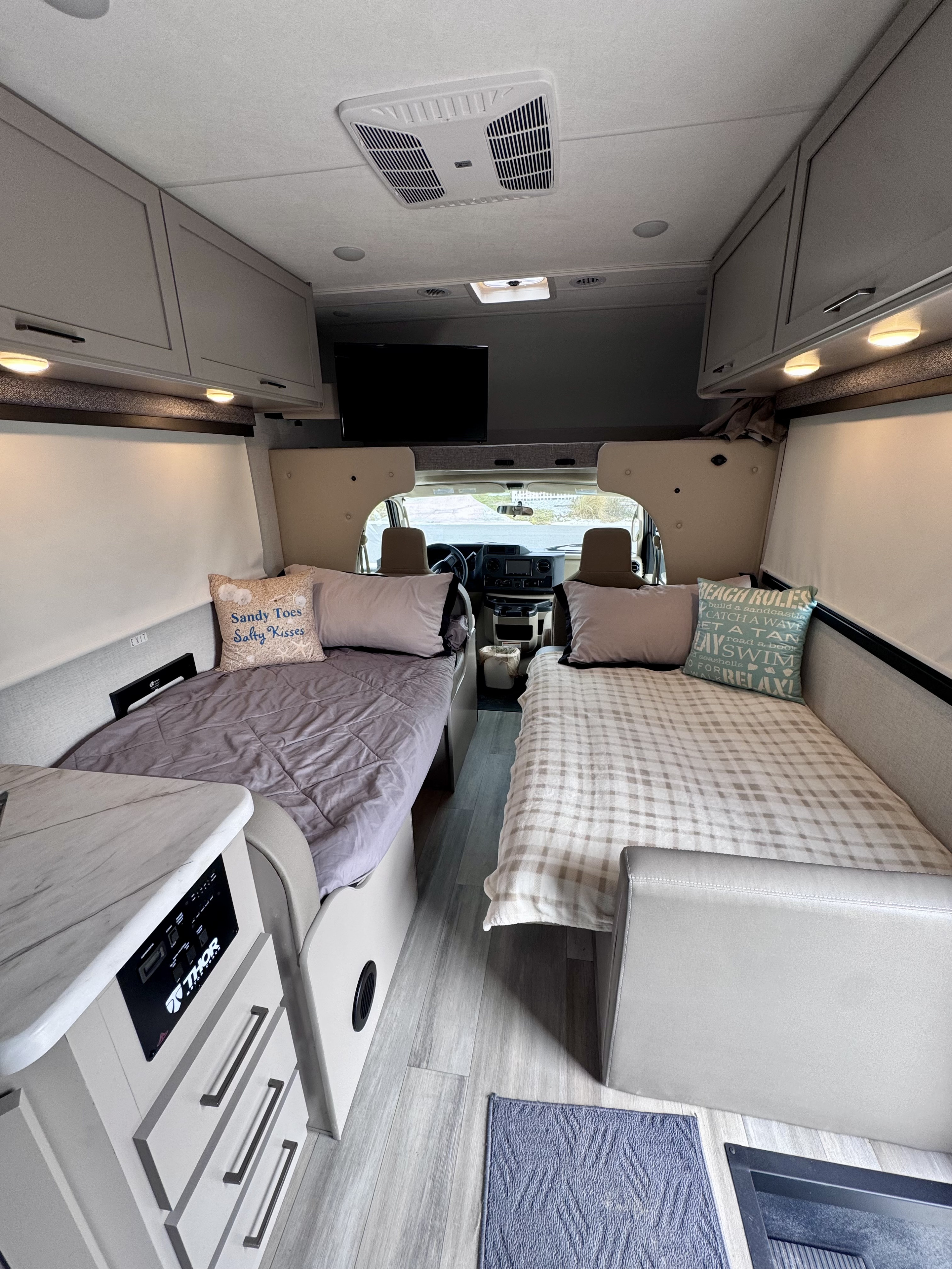Bright rv rental interior showing twin beds with beach-themed pillows, overhead cabinets, and a Thor control panel. Ready for vacation!. Thor Motor Coach 28EZF 2026