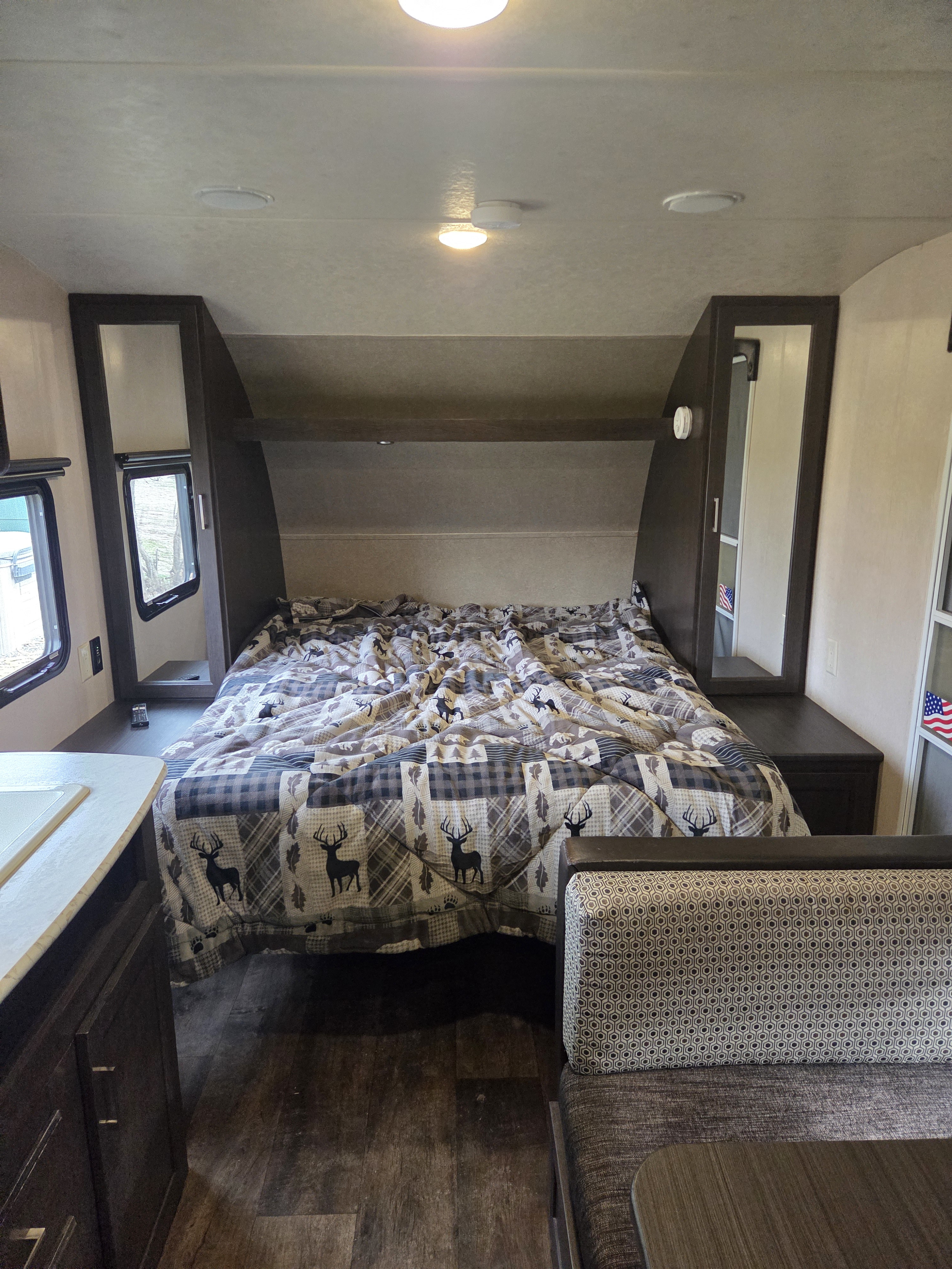 Inside this rv rental, a cozy bedroom with a deer-patterned bed, built-in storage, and dinette seating is visible.. Forest River Salem Cruise Lite 2018