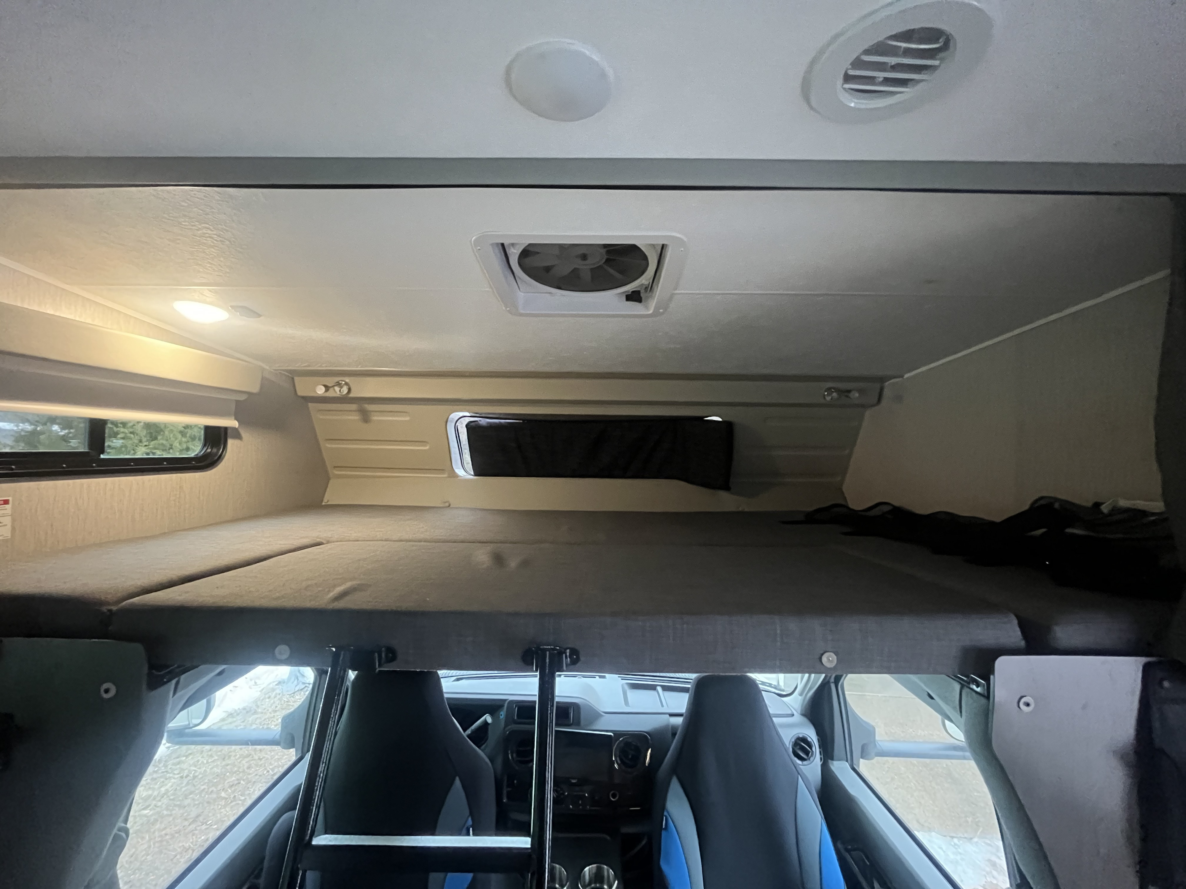 RV rental interior: Overhead bunk with mattress, ceiling fan, and AC vent. Front cabin with seats visible below the bunk.. Coachmen Leprechaun 2022