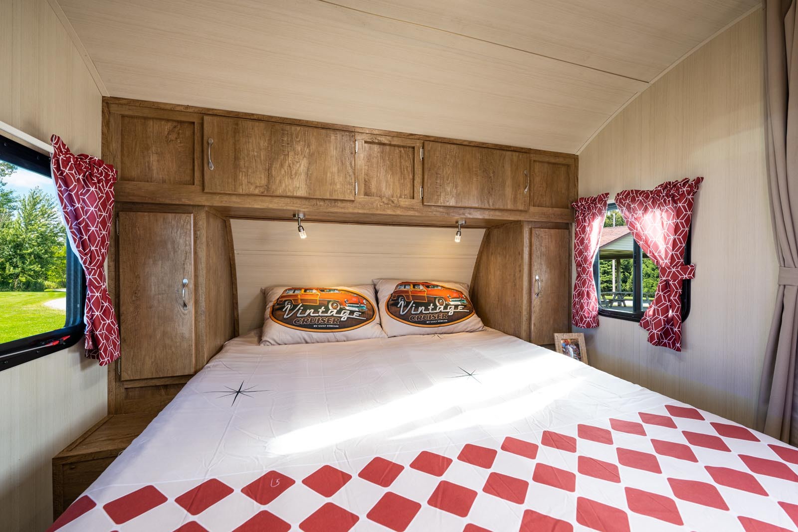 Cozy RV rental bedroom with a vintage aesthetic, featuring a comfortable bed, overhead cabinets, and sunlit windows.. Gulf Stream Vintage Cruiser 2025