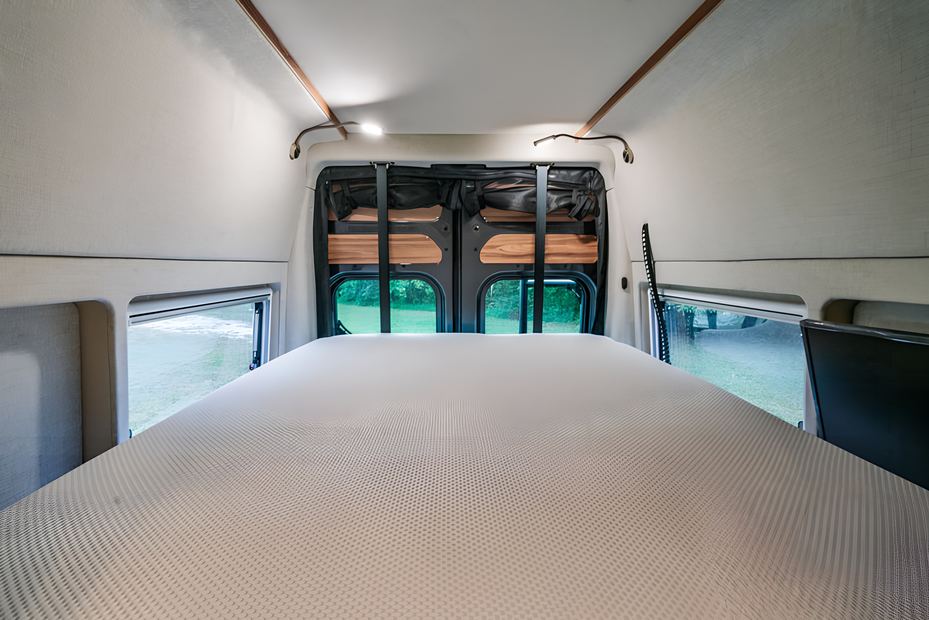 Spacious rv rental sleeping area with a comfortable bed, revealing a lush outdoor view through the back and side windows.. Noovo Plus LB 2026
