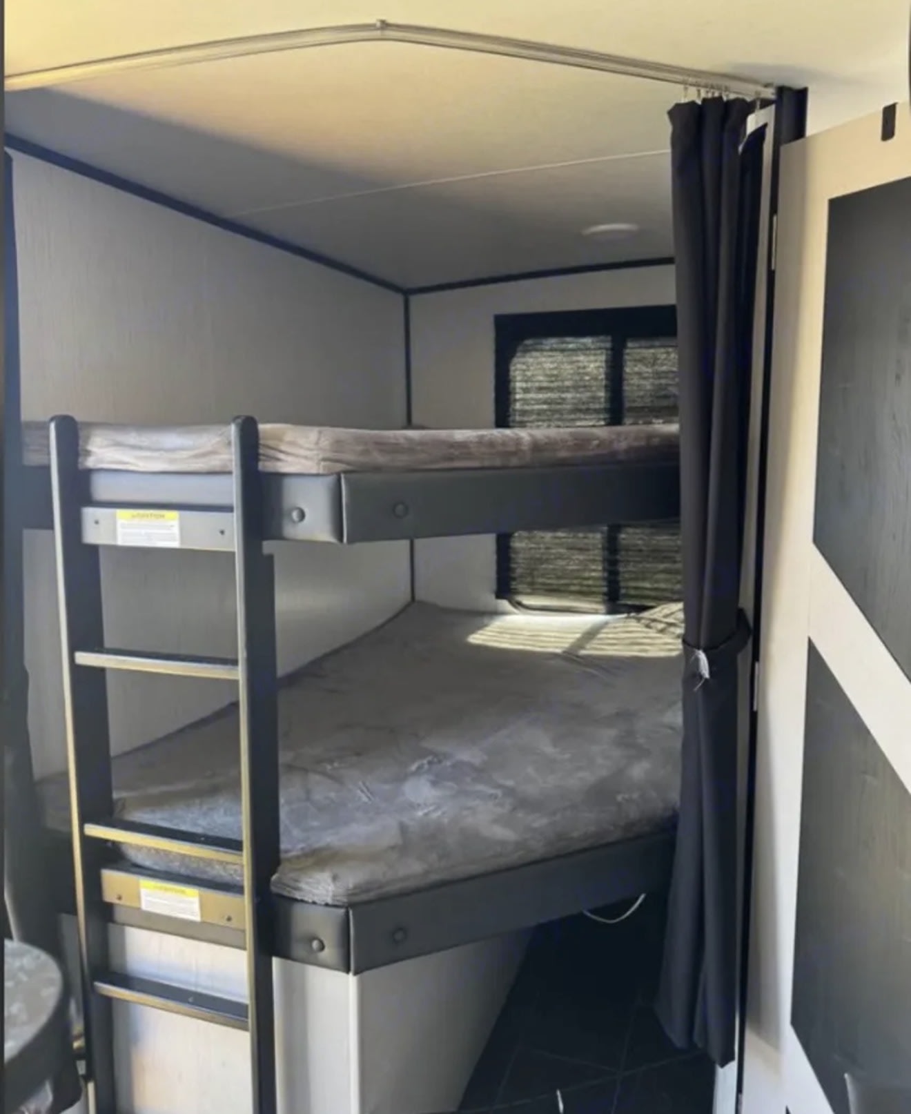 This rv rental displays bunk beds with mattresses, a ladder, and a dark privacy curtain, offering a compact sleeping area.. Heartland RVs Mallard 2022