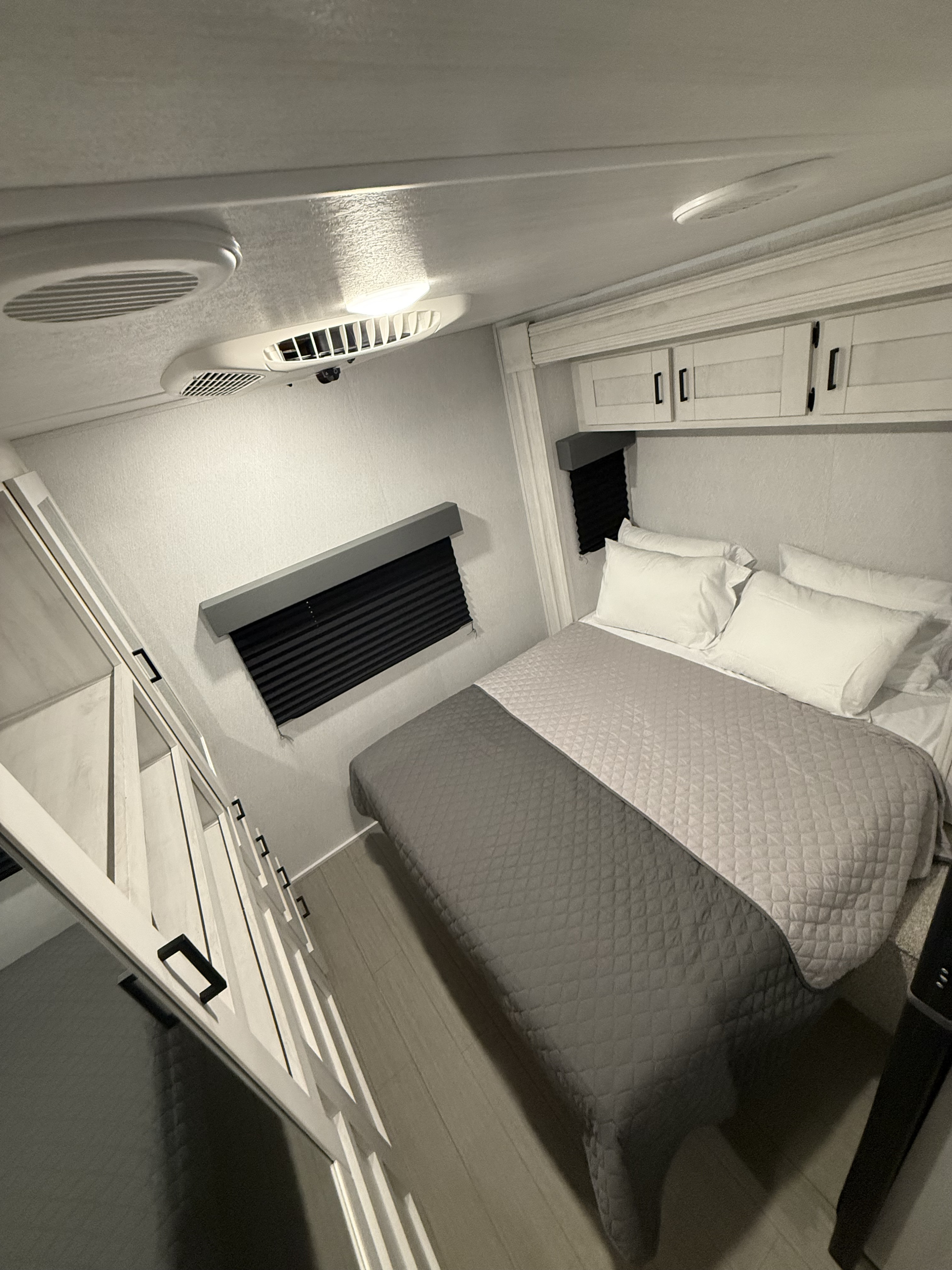 Modern RV rental bedroom: comfy bed, overhead storage, window blinds, and stairs. Your cozy retreat on wheels awaits!. East to West Entrada 2025