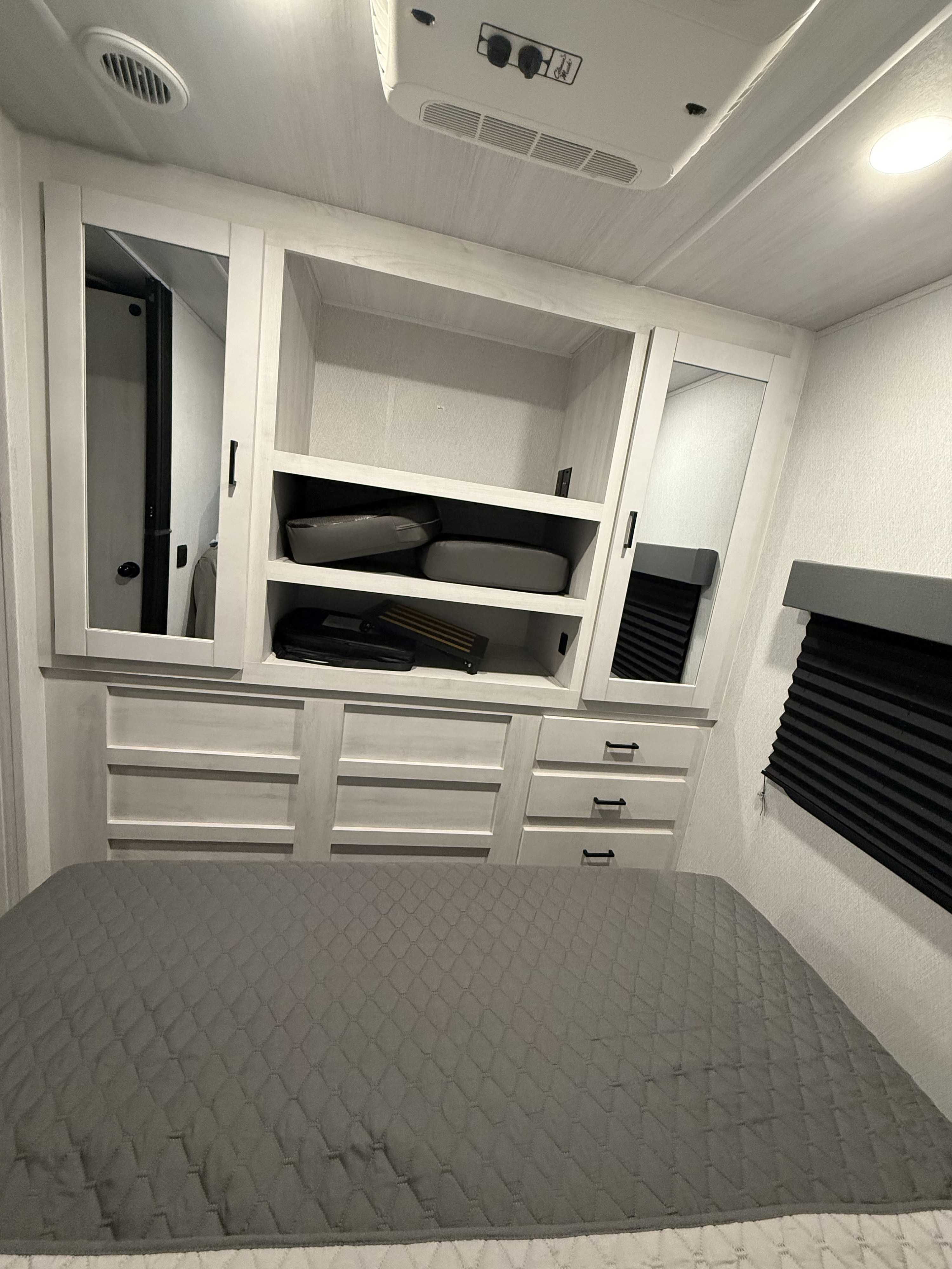 RV rental bedroom: Gray bed, light built-in cabinets with mirrors, shelves, drawers, and an overhead AC unit.. East to West Entrada 2025