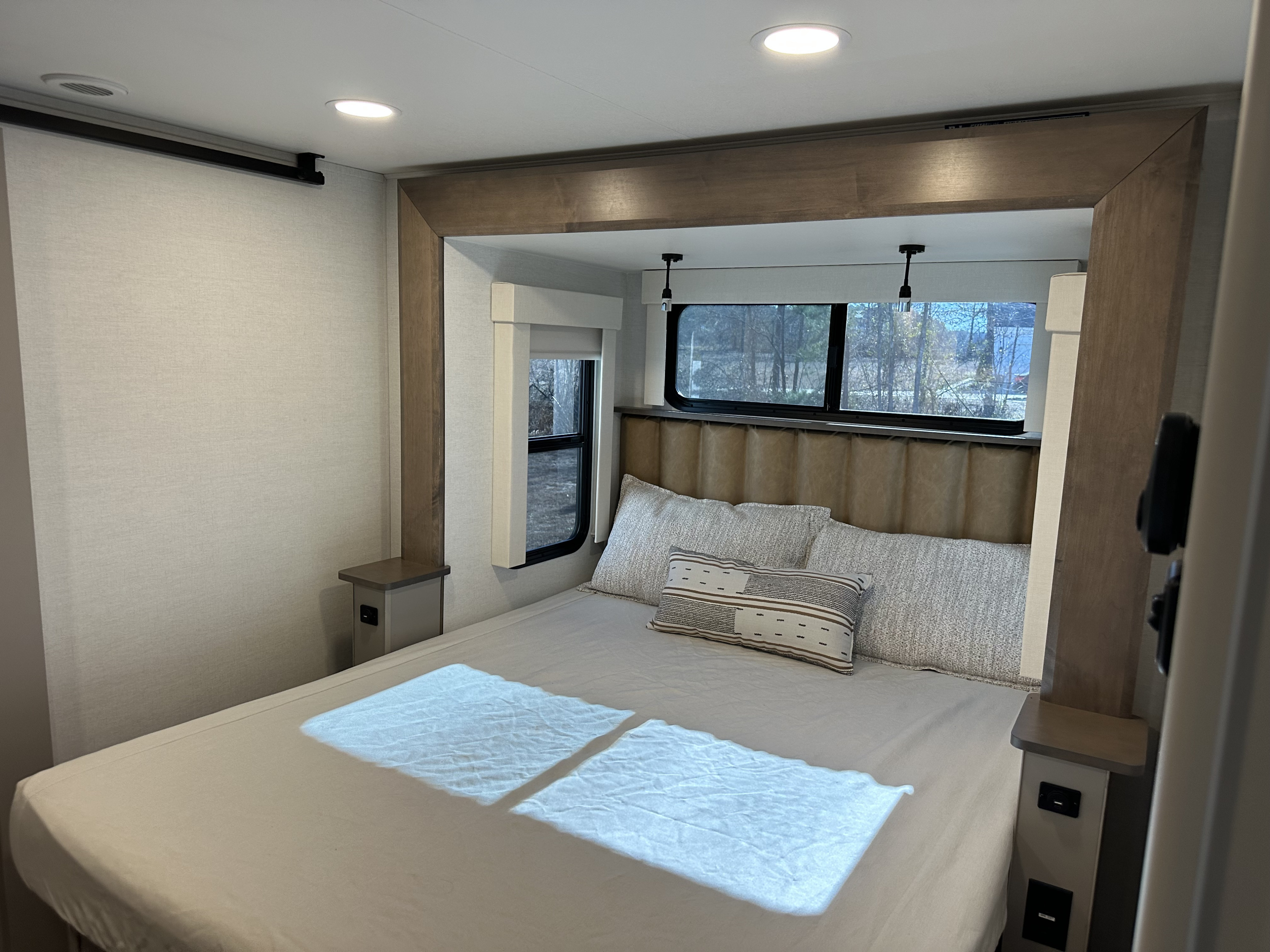 Bright RV rental bedroom features a comfy bed, windows with a view, and sleek built-in nightstands with outlets and lighting.. Alliance RV Paradigm 2025