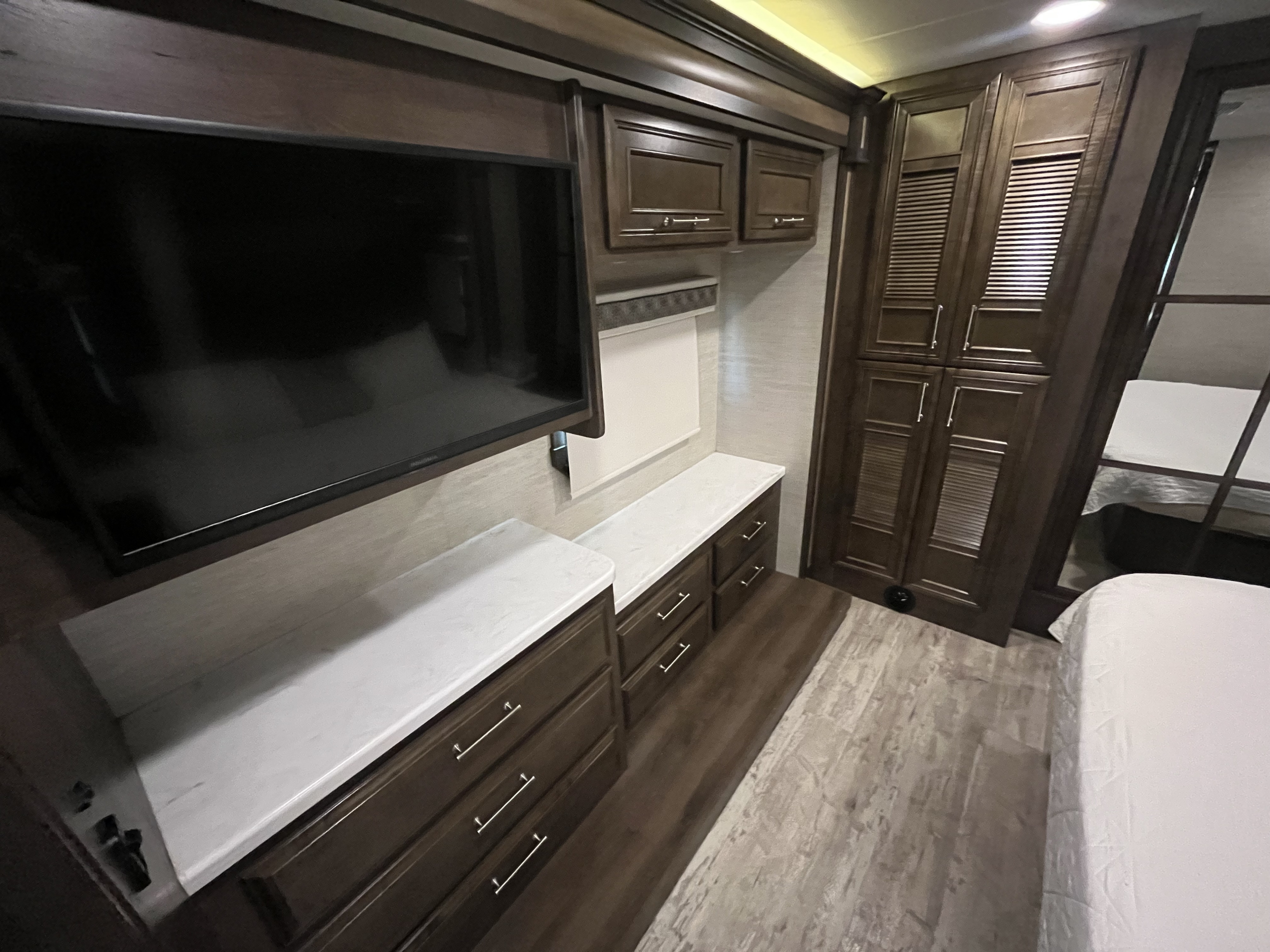 This RV rental bedroom features a flat-screen TV, dark wood cabinetry with drawers and a louvered wardrobe, and a bed.. Entegra Coach Emblem 2022