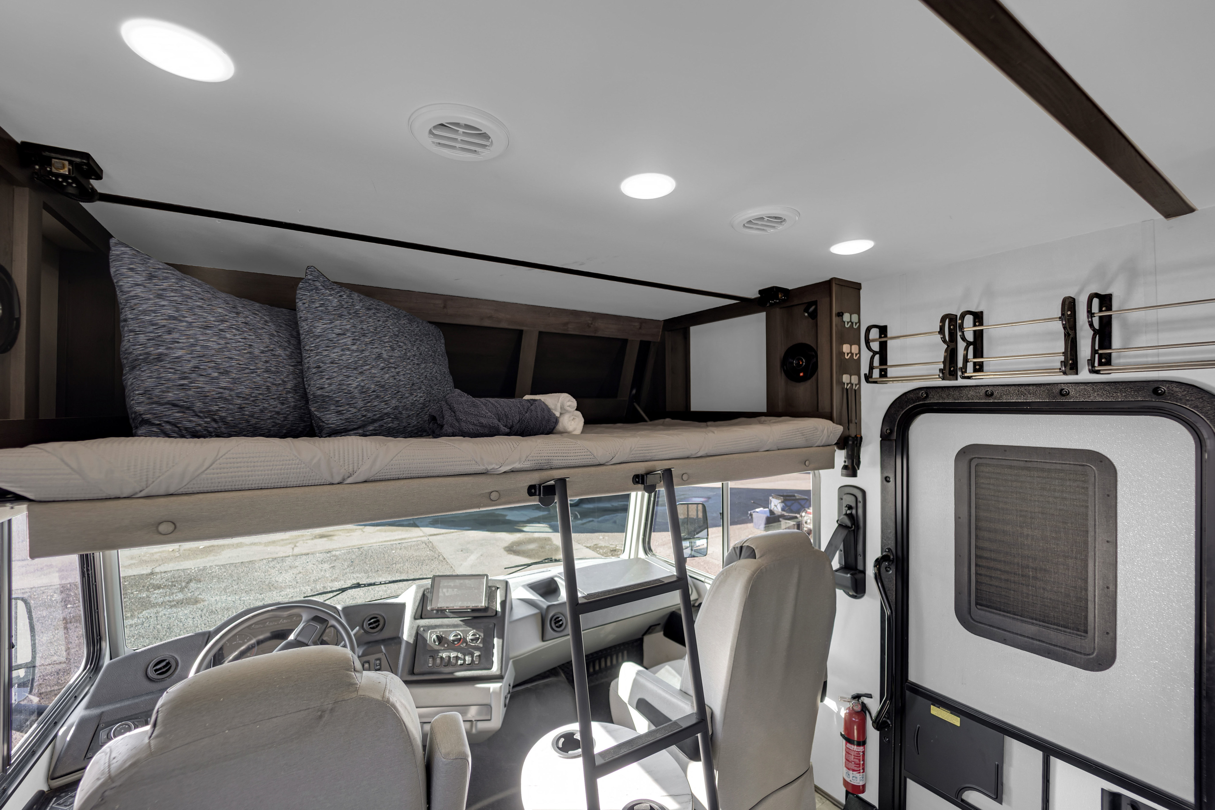 Cozy rv rental interior featuring an over-cab bunk bed, driver's cabin, and essential safety equipment like a fire extinguisher.. Forest River FR3 2021
