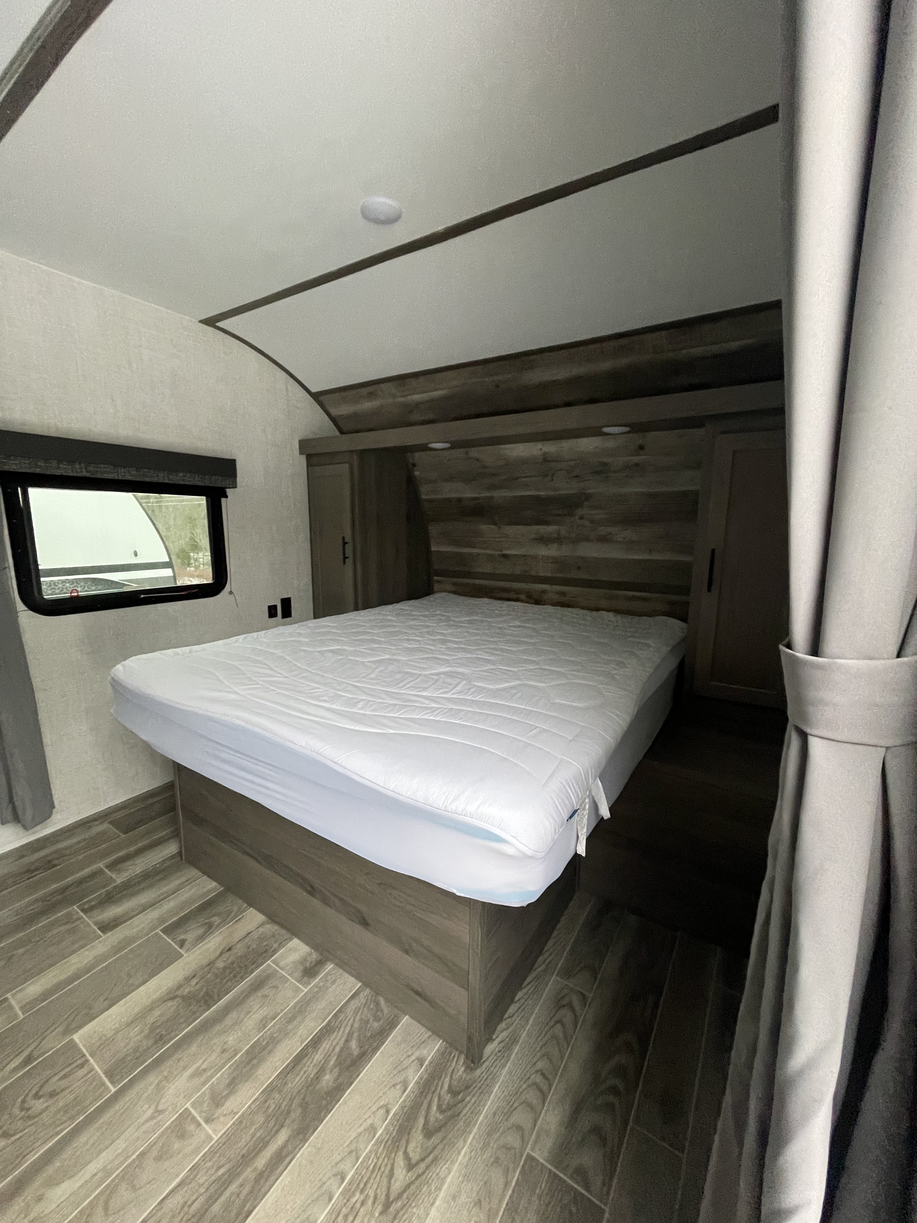 Cozy rv rental bedroom interior with a white bed, window, and stylish wood-look floor. Ready for your adventure.. Gulf Stream Friendship 2022