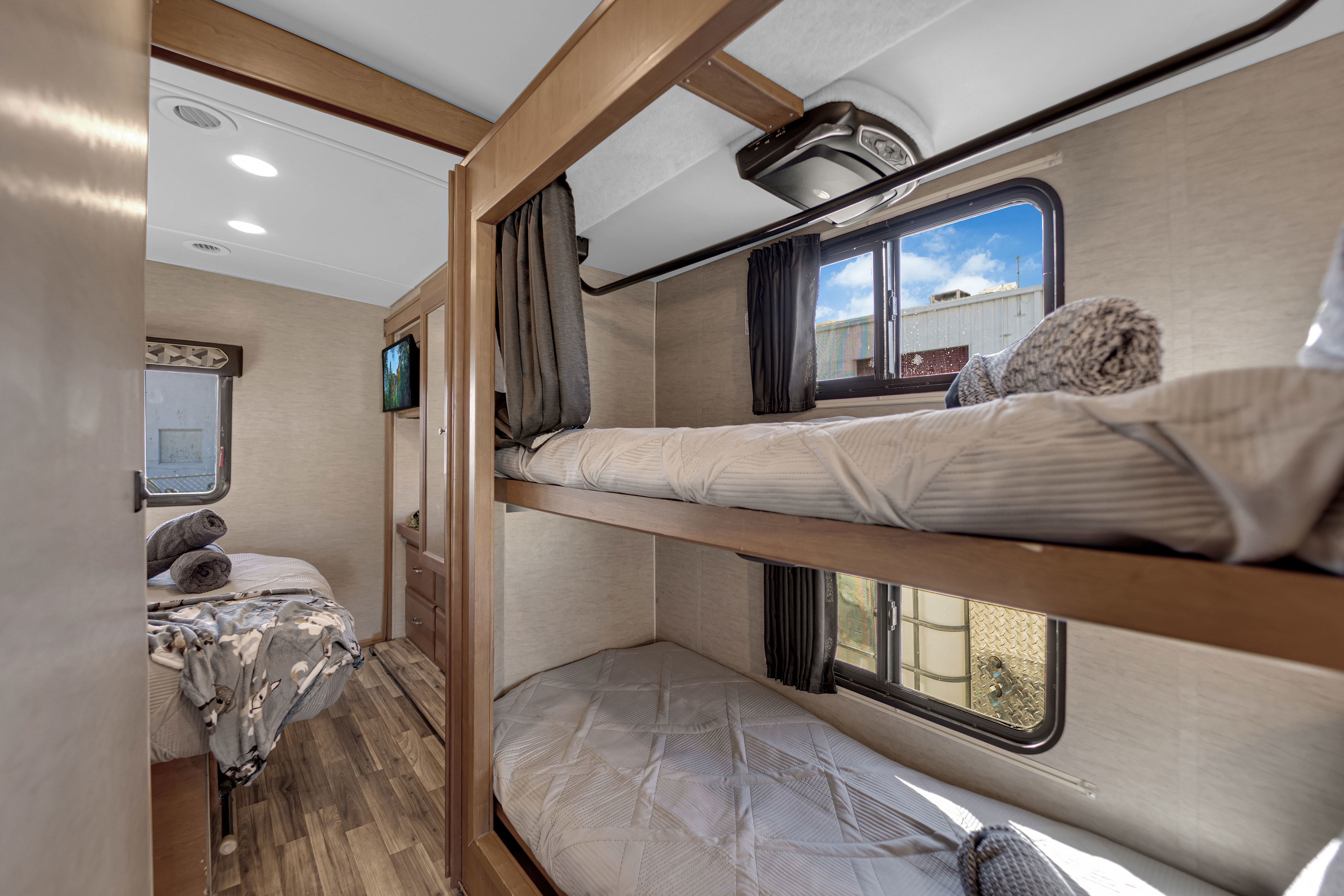 Cozy rv rental interior: bunk beds, main sleeping area with TV, and windows for natural light. Ideal for family travel.. Winnebago Vista 2017