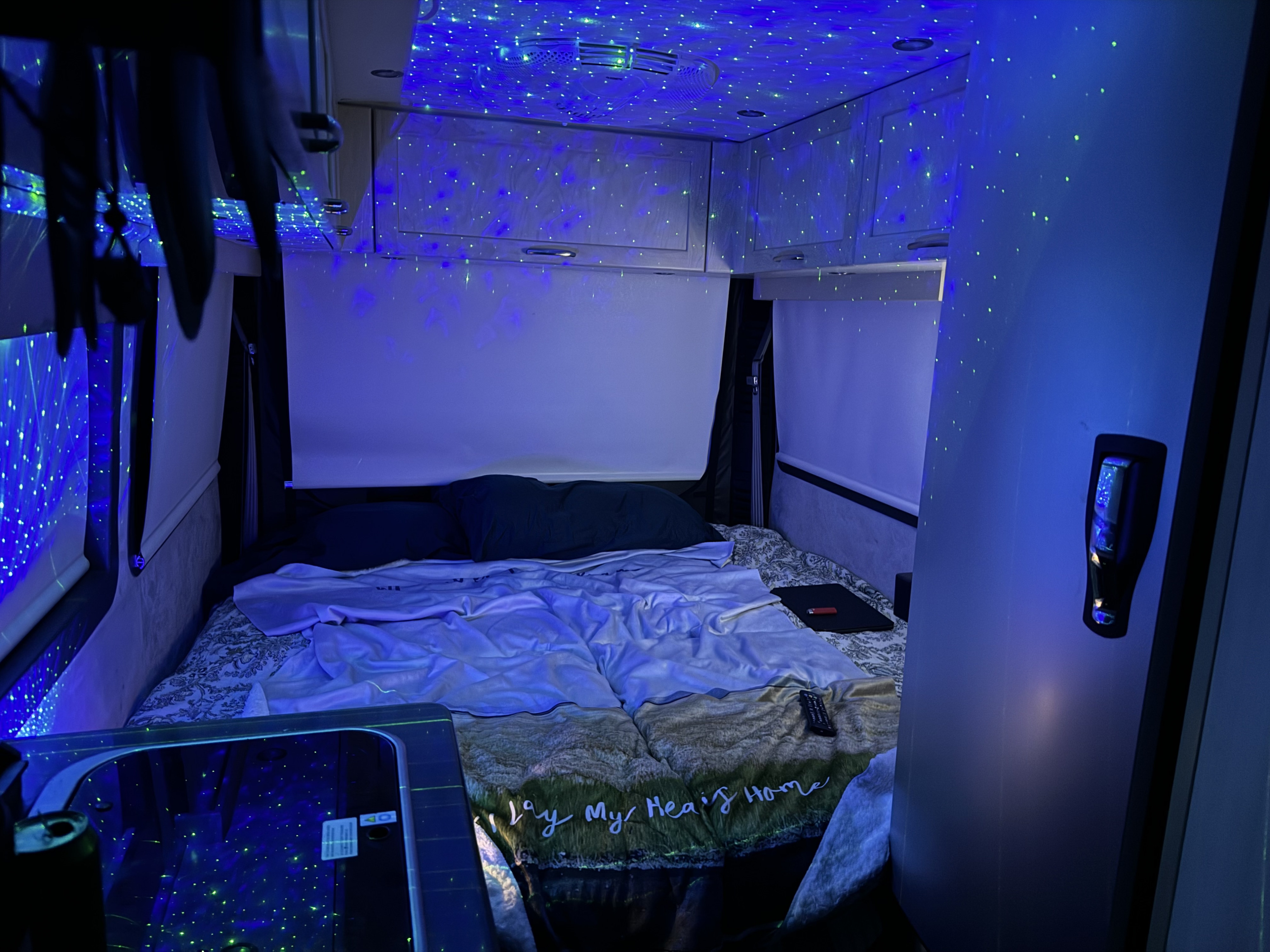 Dreamy rv rental bedroom with a galaxy of blue and green lights on the ceiling, a comfortable bed, and compact storage in this camper.. Pleasure-Way Pleasure-Way Class B 2020