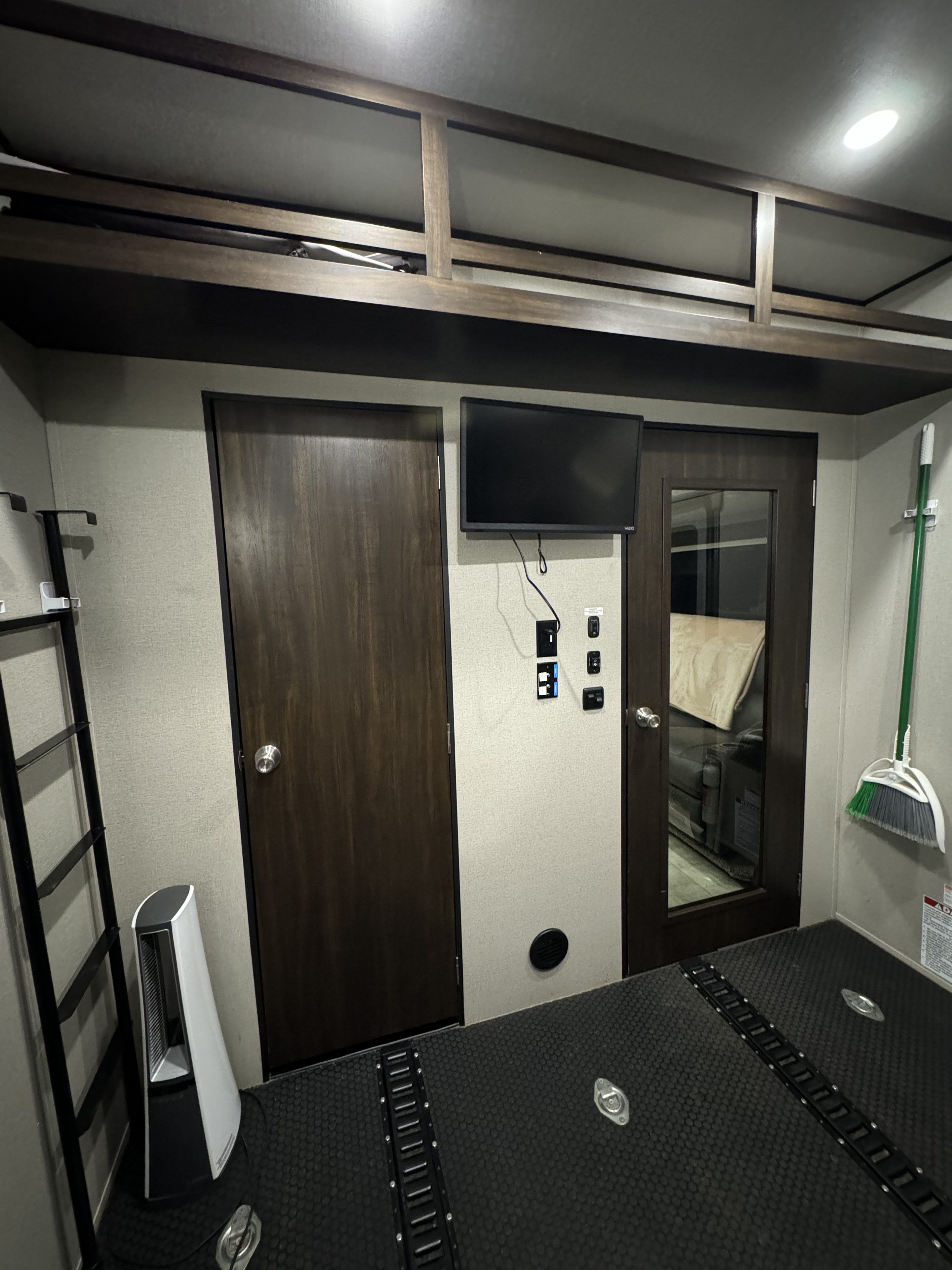 Inside a versatile rv rental toy hauler garage: textured floor, tie-downs, ladder, doors, TV, and stand-up fan.. Grand Design Momentum Toy Hauler 2020
