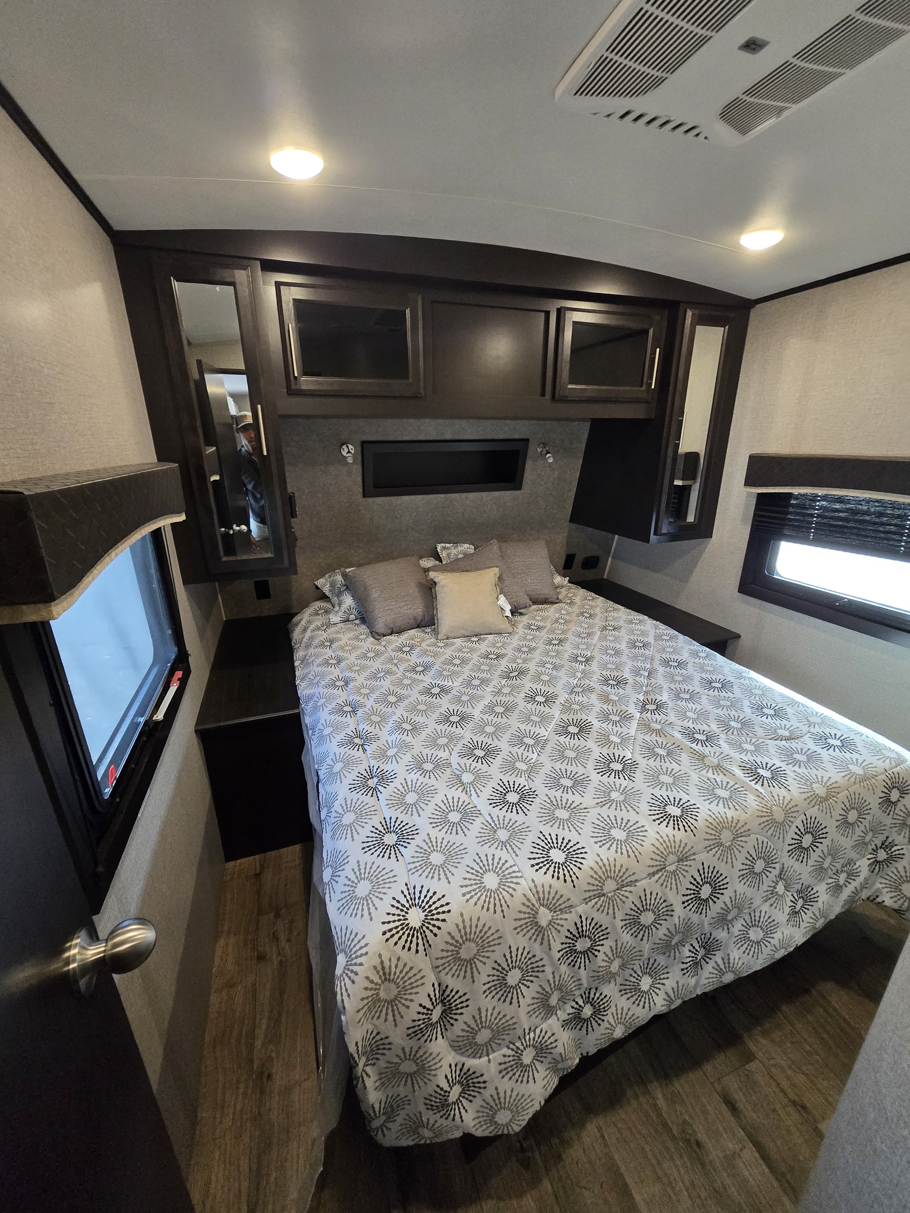 Cozy RV rental bedroom featuring a queen bed with patterned bedding, dark wood cabinets, windows, and modern lighting.. Jayco Eagle HT 2020