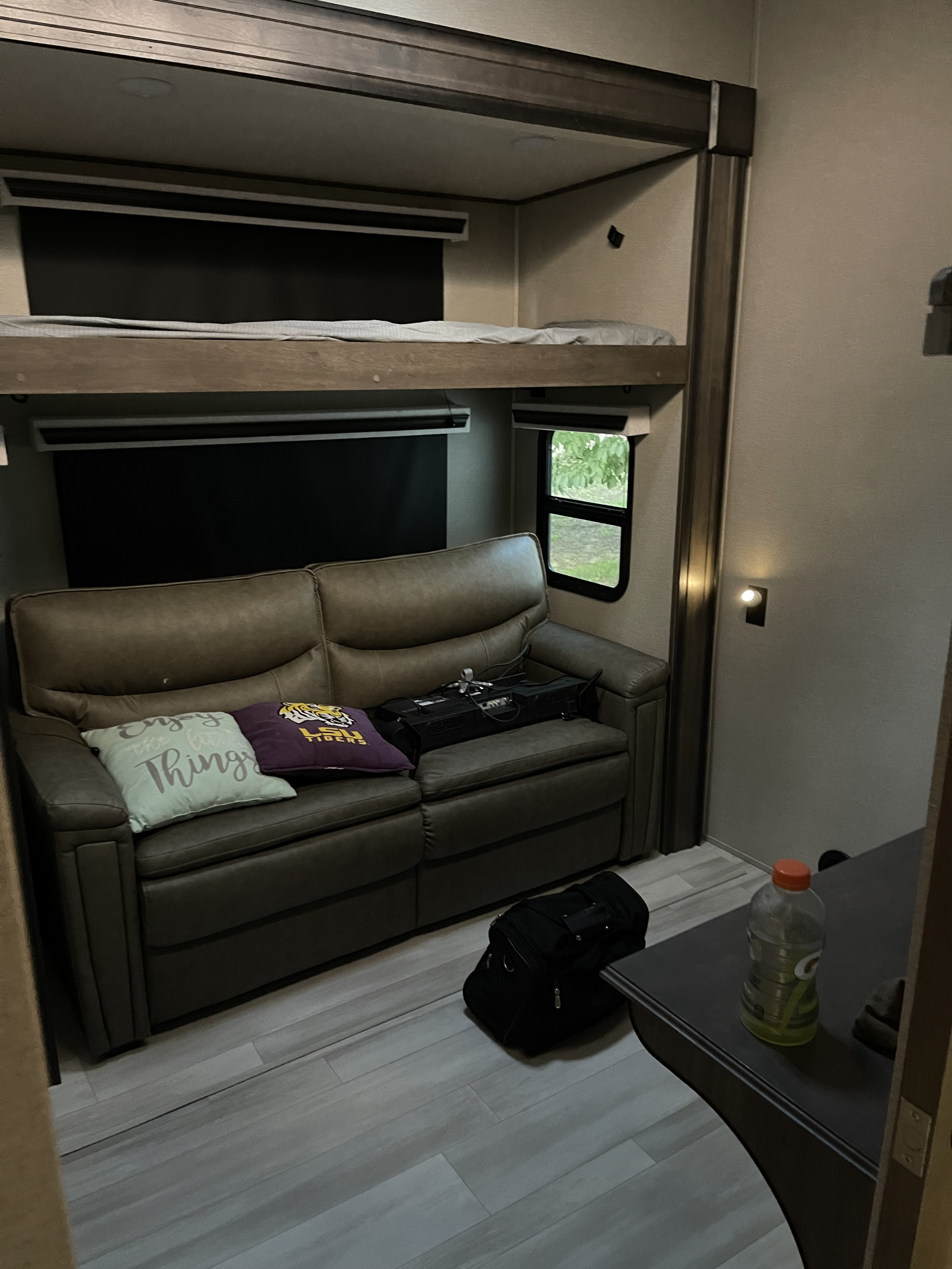 An RV rental bunkhouse area with a brown sofa, accent pillows, bunk beds, a small window, and a side table with a drink.. Grand Design Solitude 2022