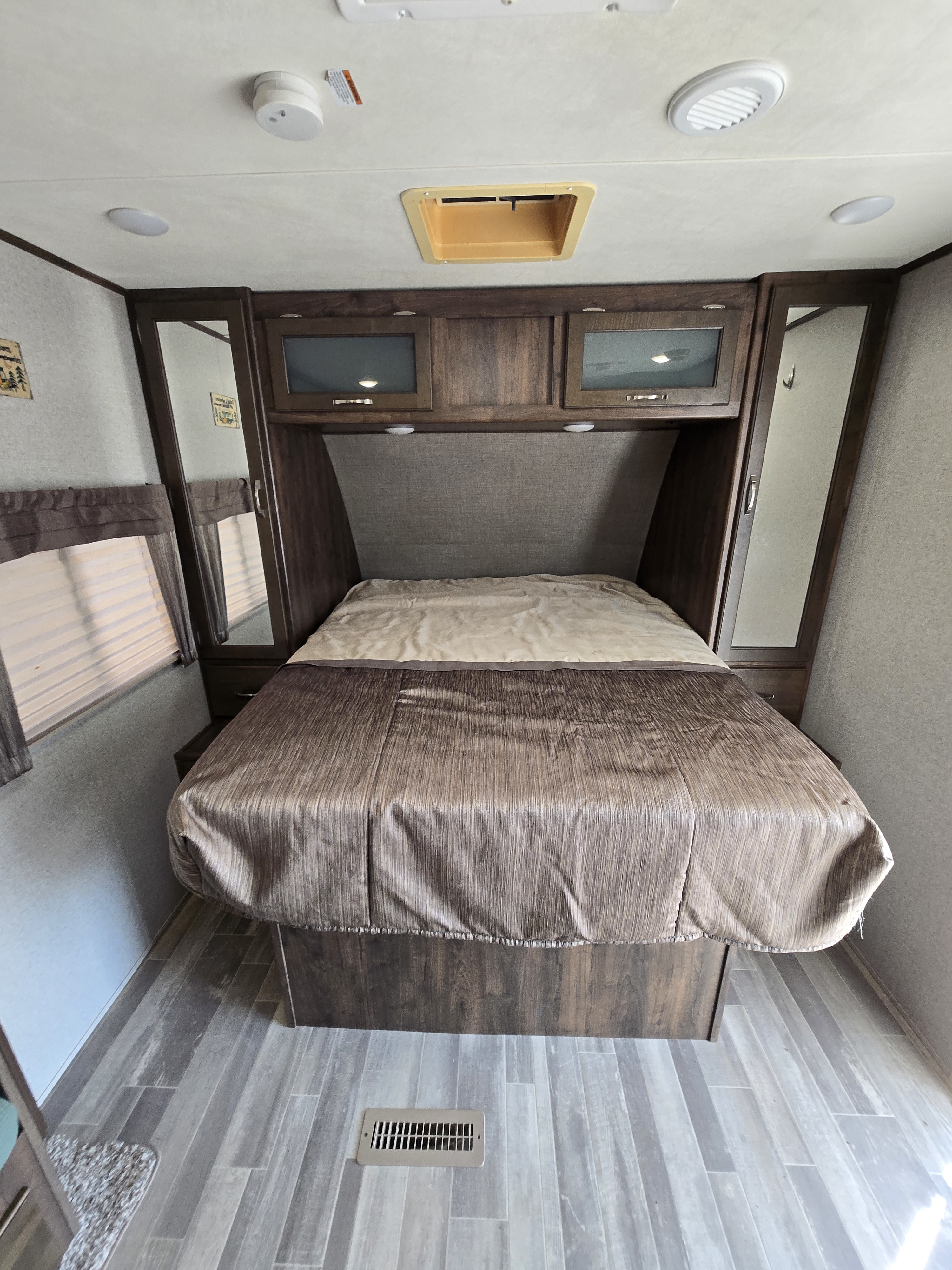 This RV rental bedroom offers a comfortable bed, cabinets, mirrors, and window blinds in a compact, functional space.. Coachmen 2133RB 2019