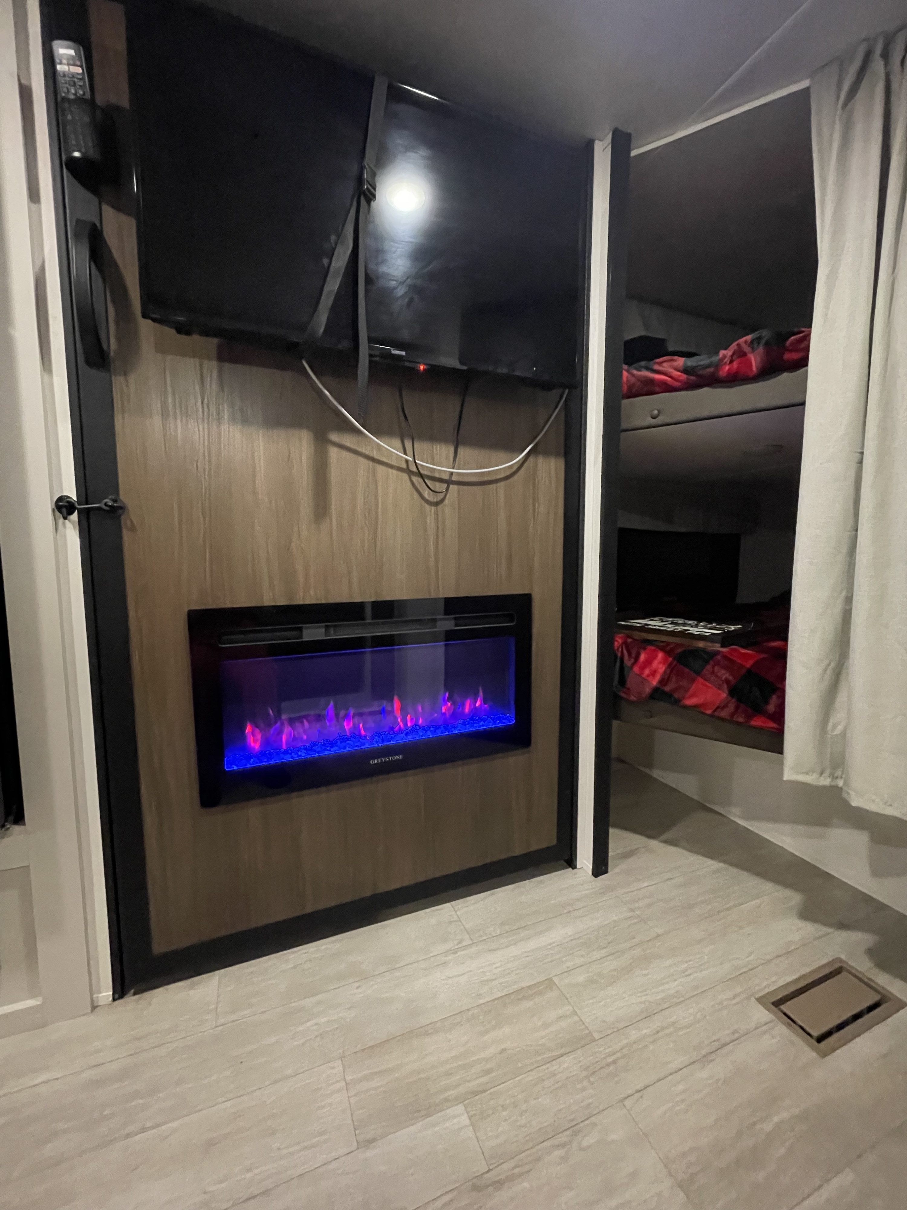 Inside a cozy rv rental, featuring a mounted TV, an electric fireplace with colorful flames, and bunk beds with plaid covers.. Forest River Prime Time Avenger 2026