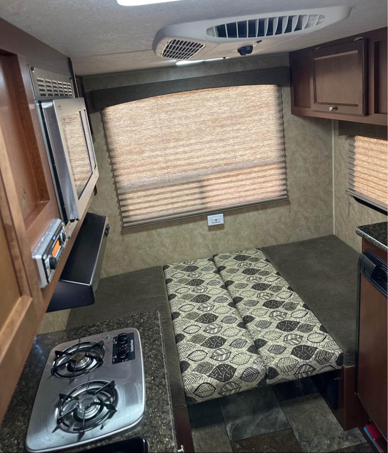 Explore this RV rental's compact interior: two-burner stove, microwave, and a cozy leaf-patterned bed area.. Coachmen Clipper 2016