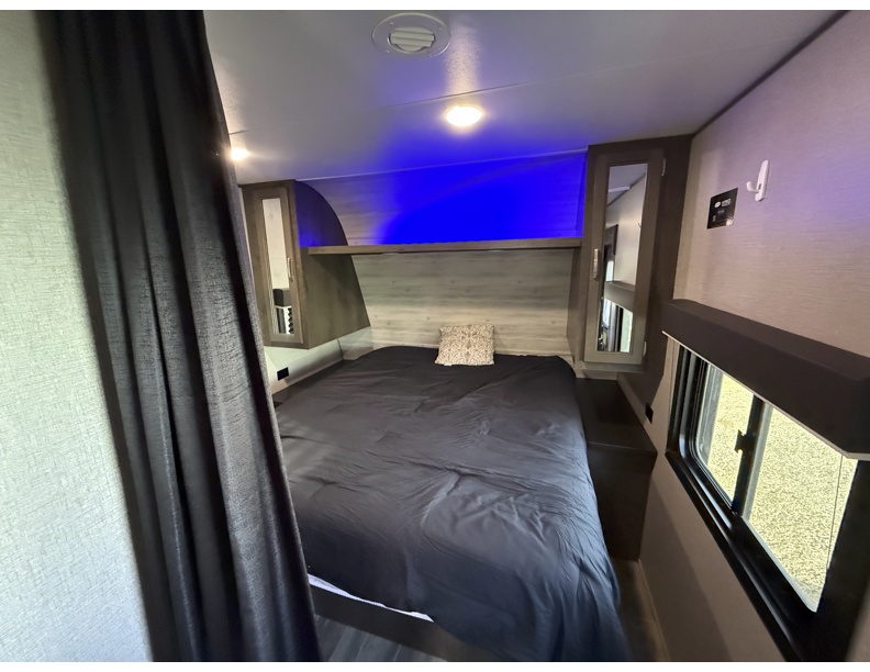 Inside this RV rental, a cozy bedroom with a dark bed, blue accent lighting, side cabinets, and a window.. Jayco Jay Flight 2021