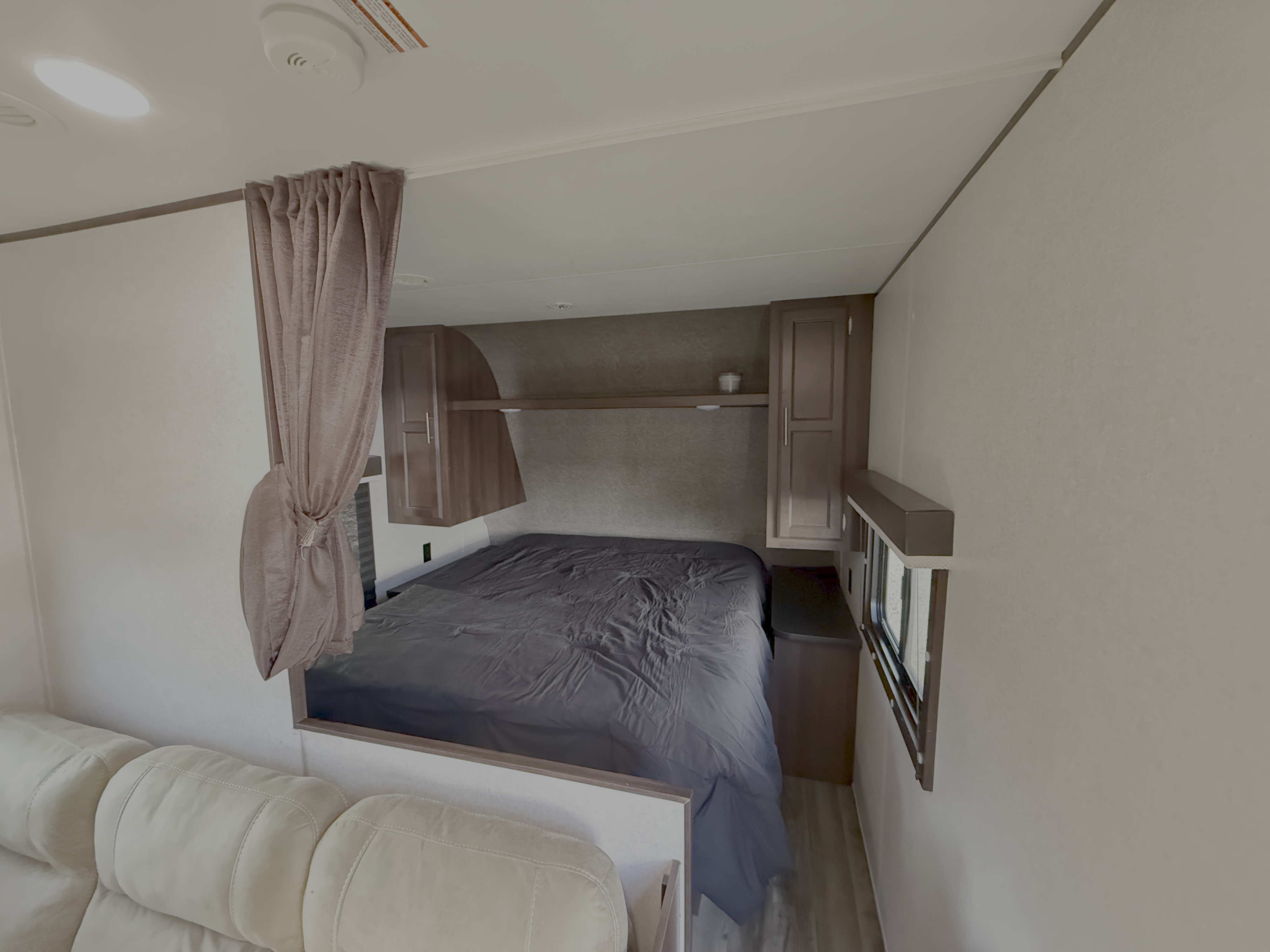 RV rental bedroom with dark bed, wood cabinets, a privacy curtain, and a peek of a cream sofa. Compact and inviting.. Jayco Jay Flight SLX 2019