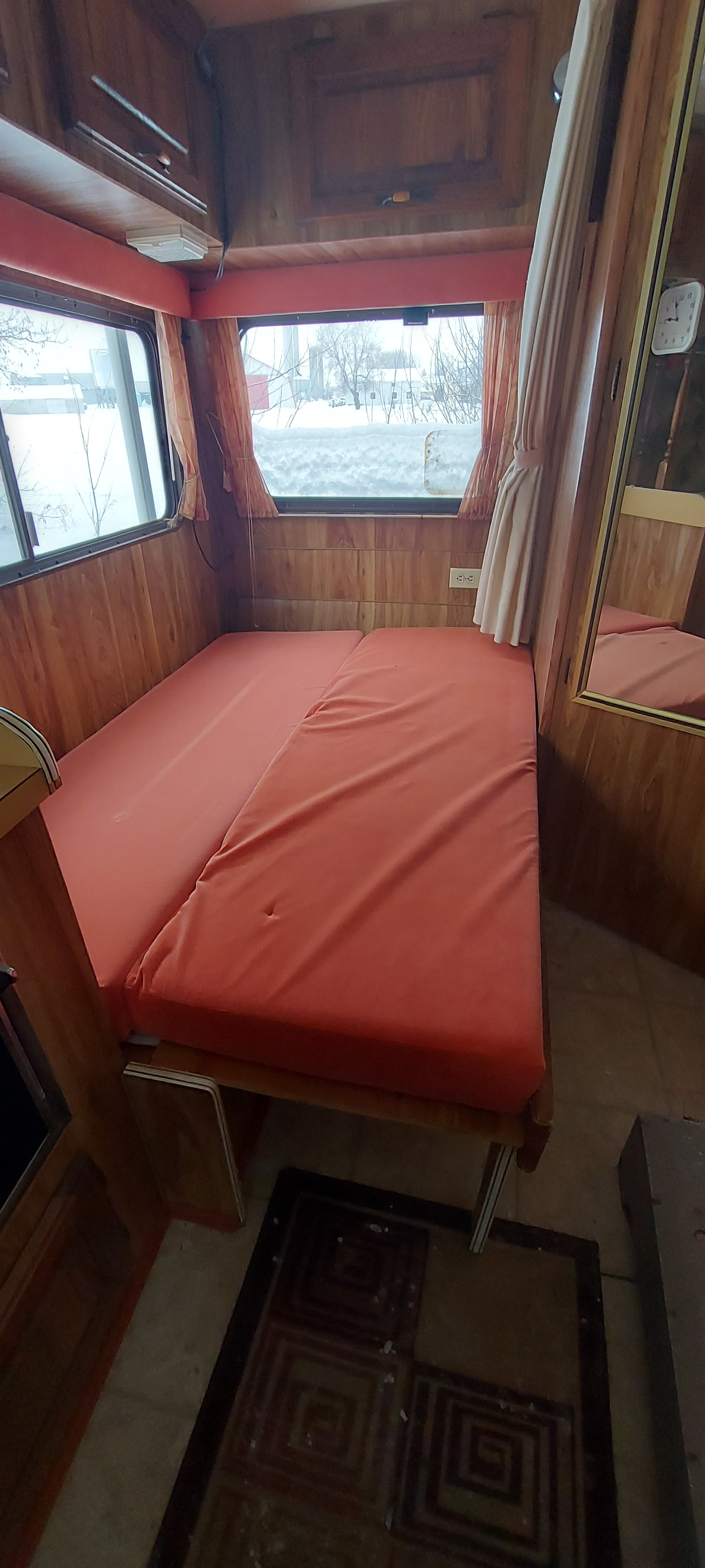 Cozy vintage RV rental interior featuring a fold-out bed, wood paneling, and large windows overlooking a snowy landscape.. Ford FORD CTV 1985