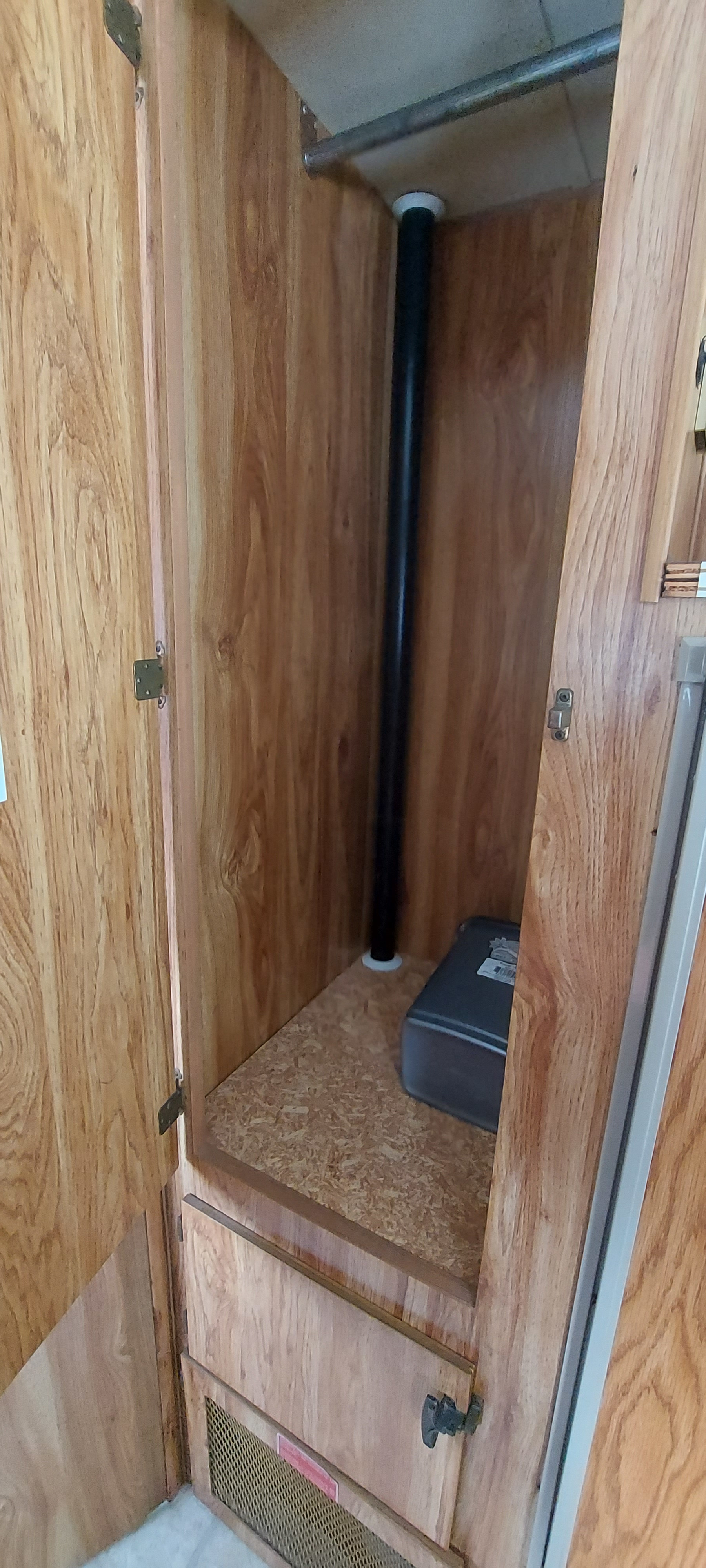 RV rental closet with wood-paneled interior, hanging rod, central pipe, and a storage box on the lower shelf.. Ford FORD CTV 1985