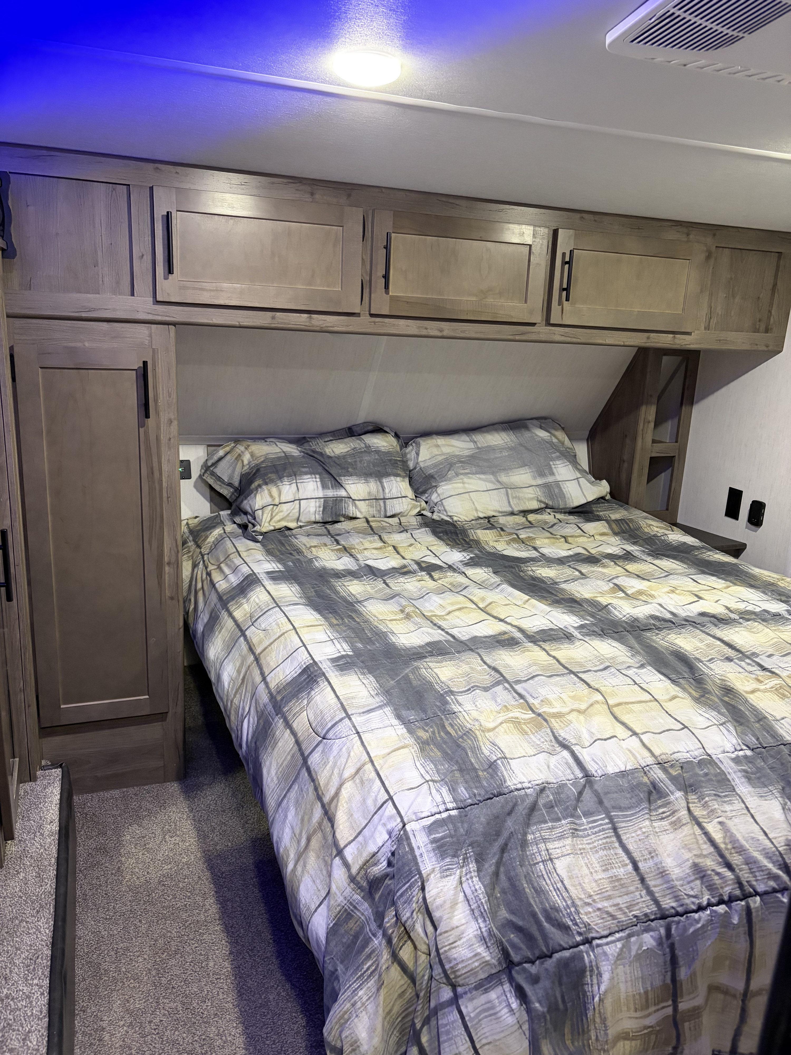 RV rental bedroom: cozy space with plaid bedding, overhead cabinets, and built-in bedside storage for convenience.. Forest River Cherokee Wolf Pack Toy Hauler 2020
