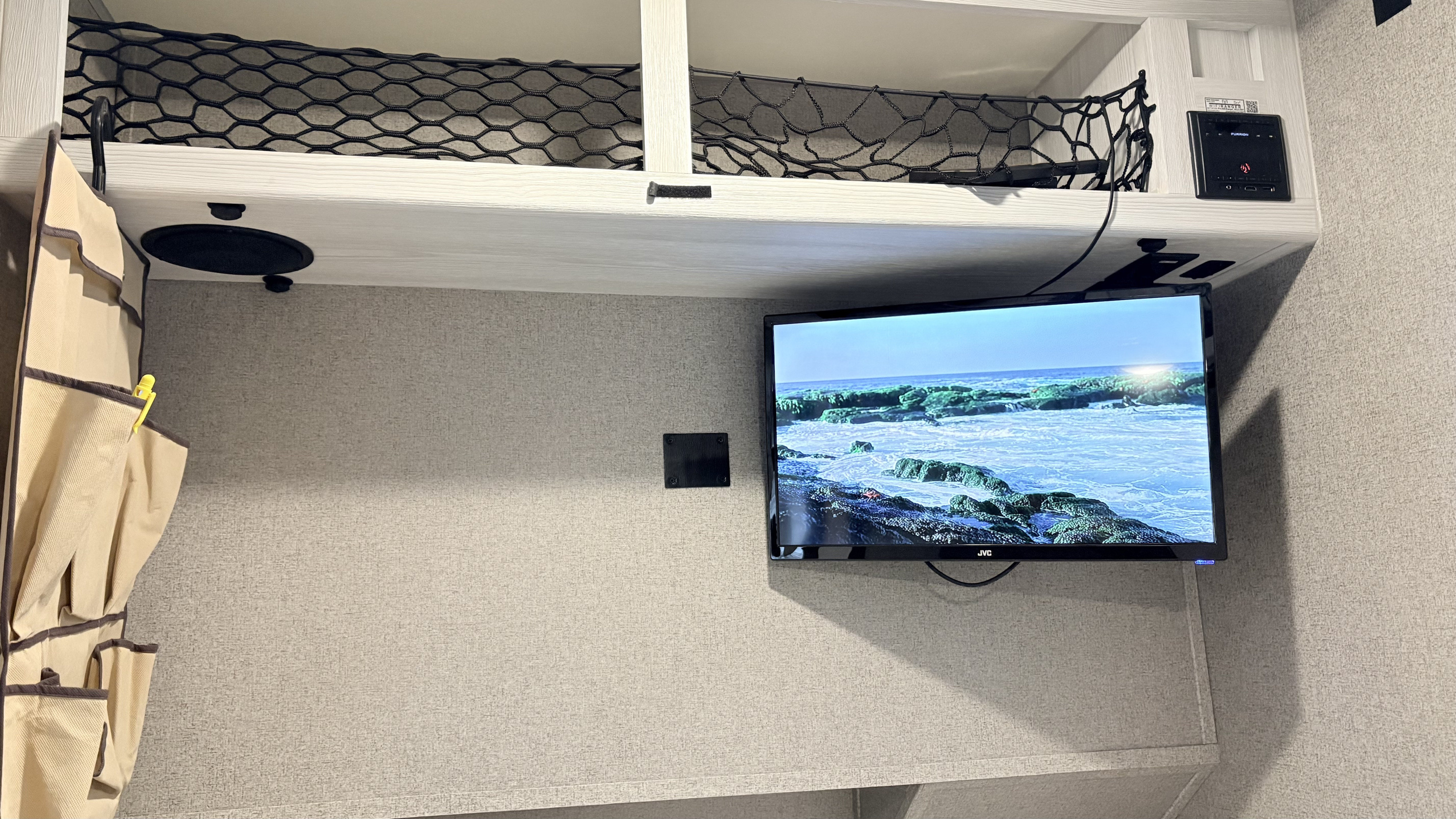 RV rental interior with JVC TV, Furrion panel, overhead bunk with net storage, and a fabric wall organizer.. Forest River Rockwood Geo Pro 2018