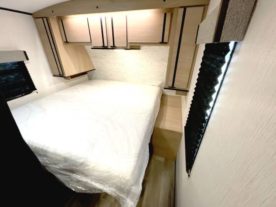 RV rental bedroom: cozy interior with new bed, small window with blinds, and sleek overhead storage.. Cruiser RV Radiance 2023