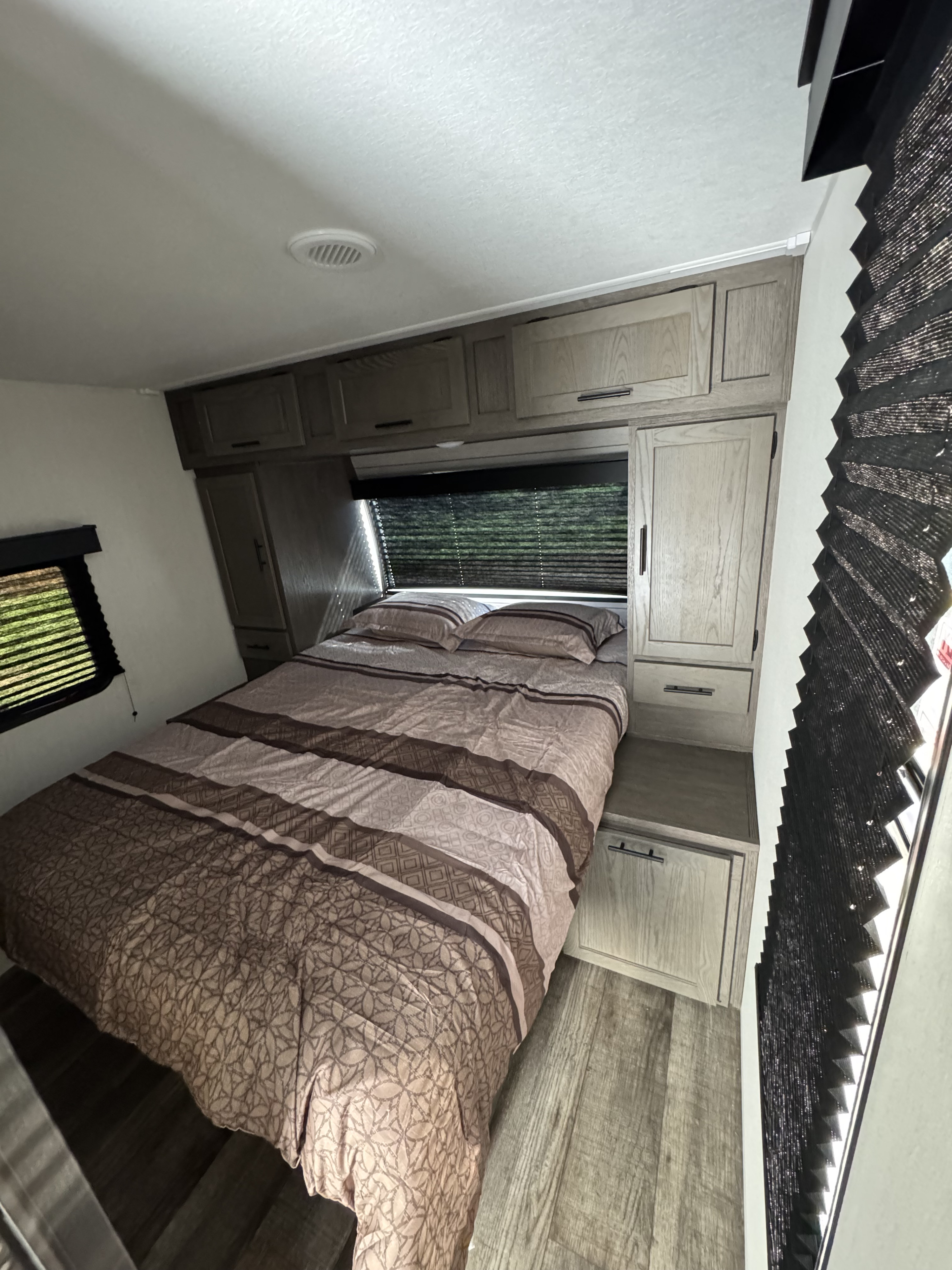 Relax in this RV rental bedroom with cozy patterned bedding, built-in cabinets, and privacy blinds.. Forest River Cherokee Alpha Wolf 2025