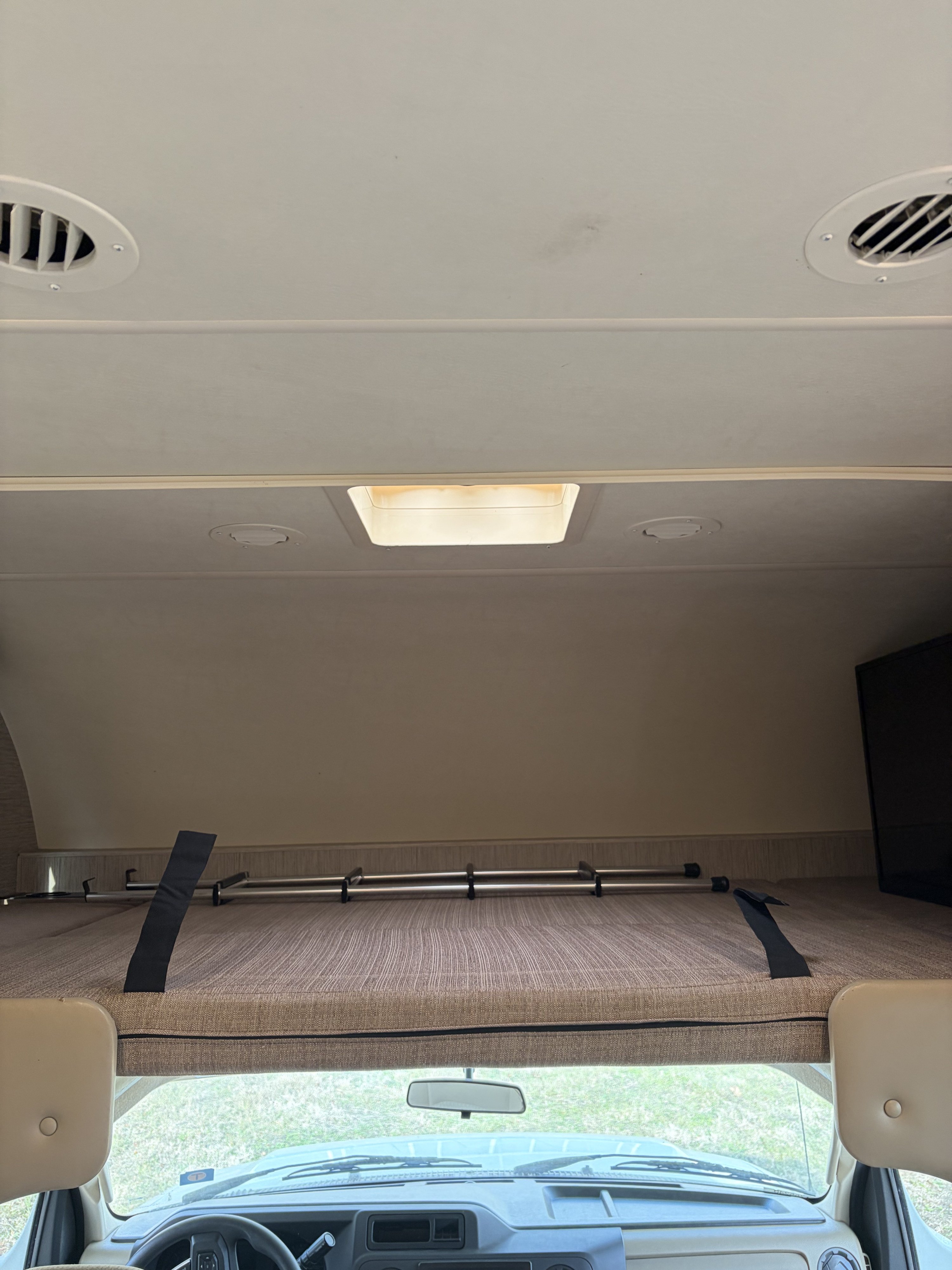 Inside an rv rental: View of the cab-over bunk bed with safety railing, driver's area, ceiling vents, and skylight above.. Thor Daybreak 2021