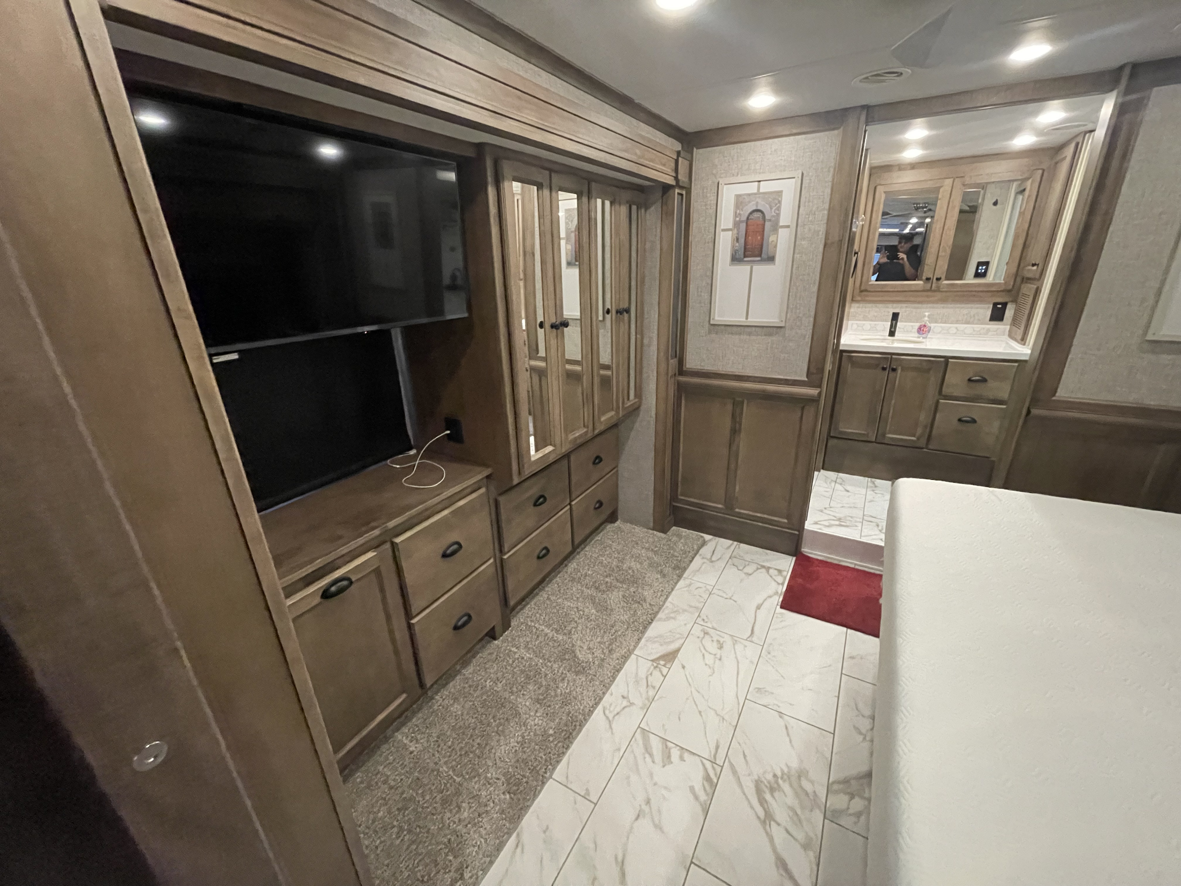 Modern rv rental bedroom with TV, mirrored wardrobe, and private vanity bathroom. Features wood cabinetry and mixed flooring.. Tiffin Allegro Bus 2025