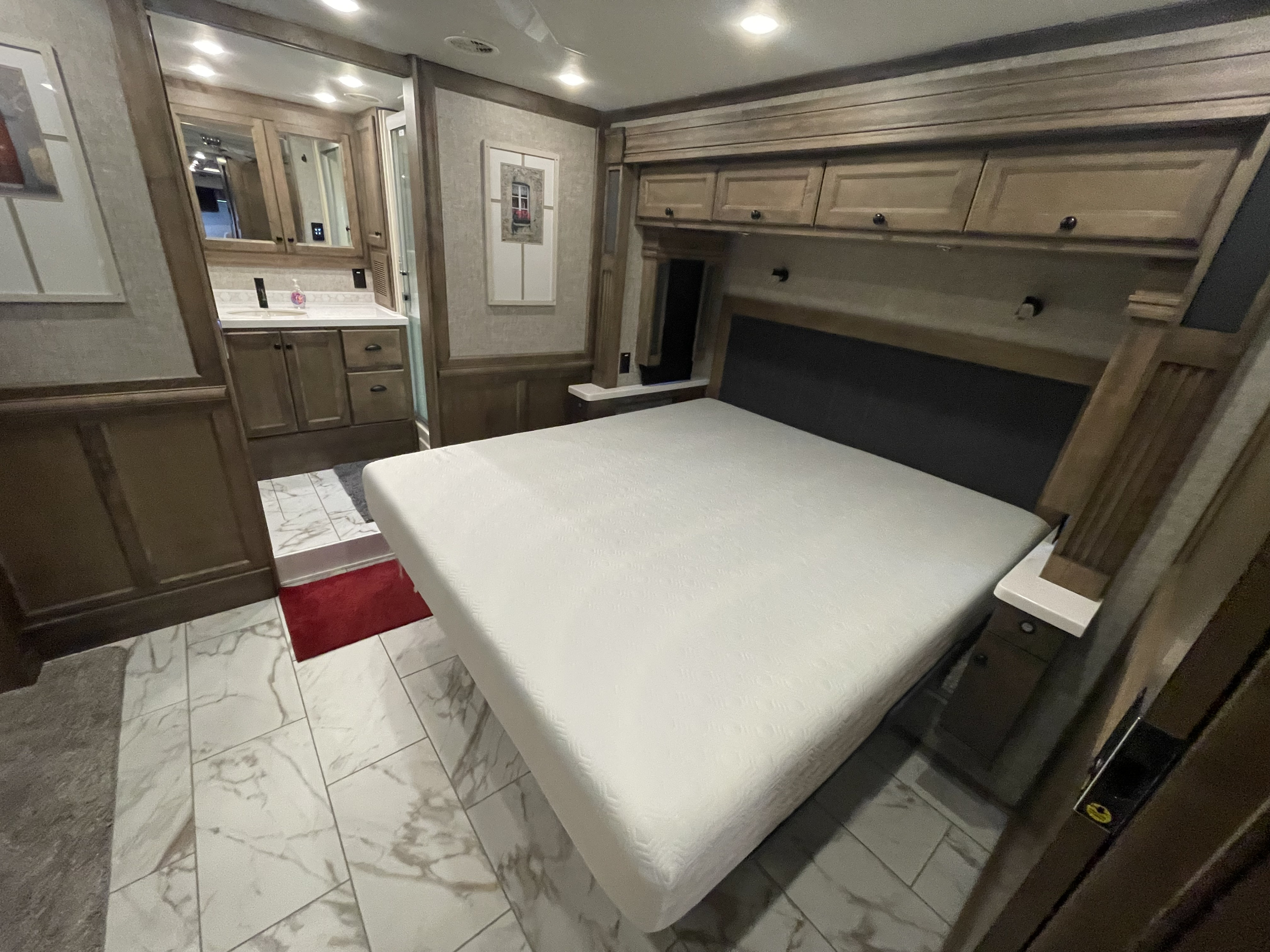 Modern RV rental bedroom: features a large, comfortable bed, overhead wood cabinetry, and an adjoining tiled bathroom.. Tiffin Allegro Bus 2025