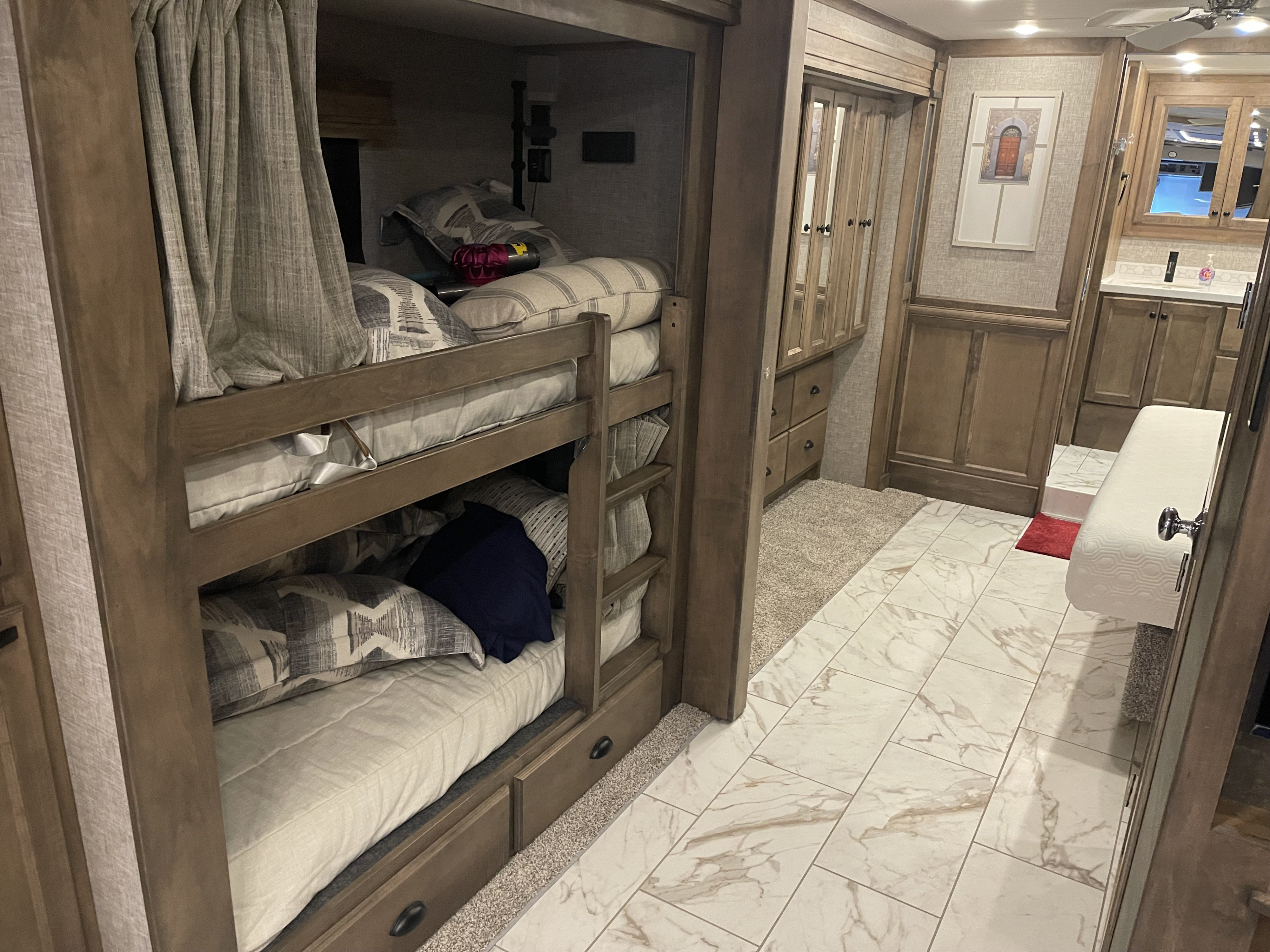 Modern rv rental bunk beds and interior hallway with cabinets, a small bathroom vanity, and stylish tiled floors. Perfect for families.. Tiffin Allegro Bus 2025