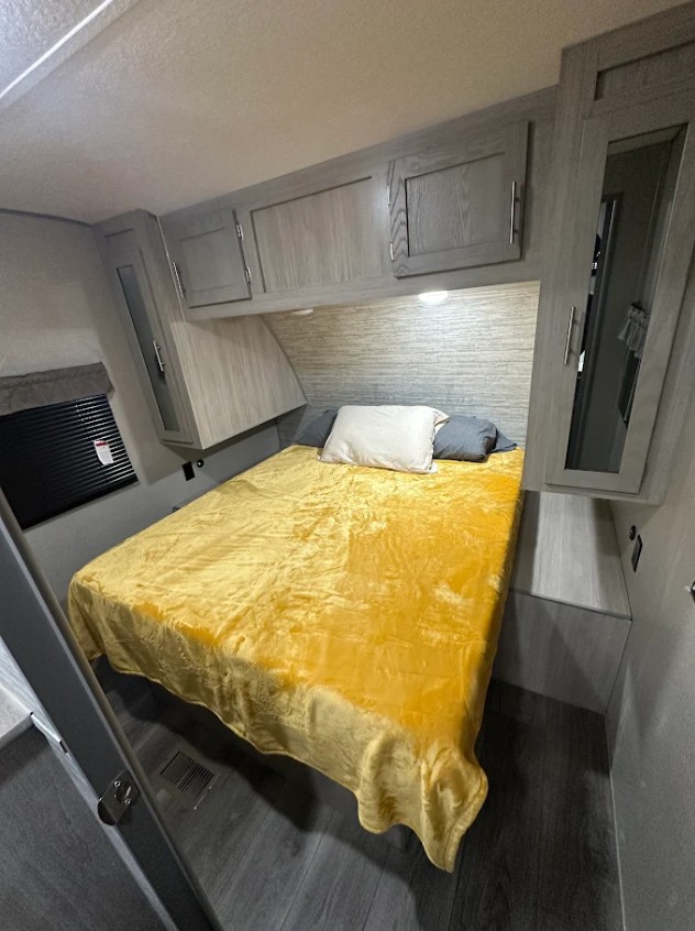Inside an rv rental: a well-appointed bedroom with a bright yellow bedspread, gray wood-look cabinets, and clever storage solutions.. Forest River Coachmen Catalina Legacy 2022