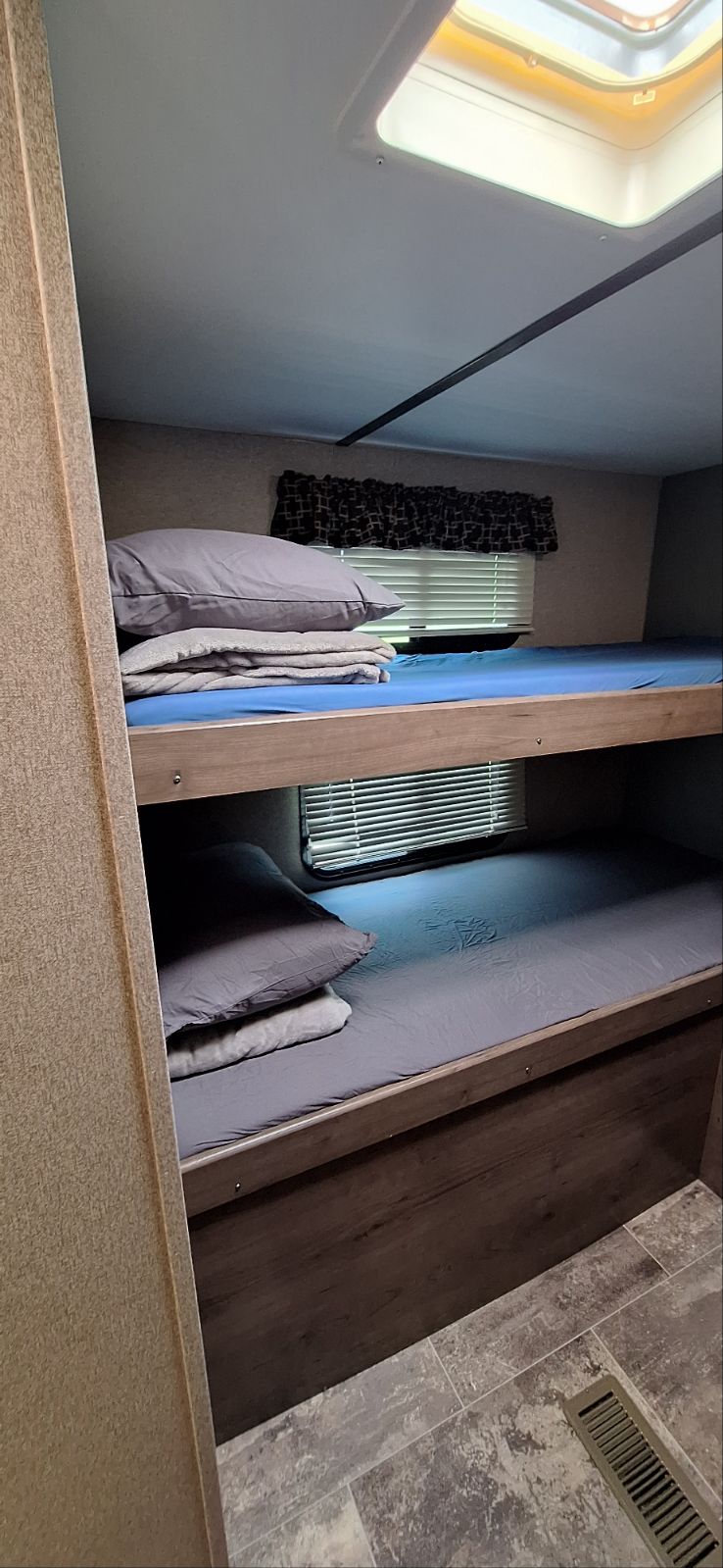 RV rental interior: comfy bunk beds with blue and gray sheets, pillows, windows with blinds, and a ceiling skylight.. Passport 3220BH 2018