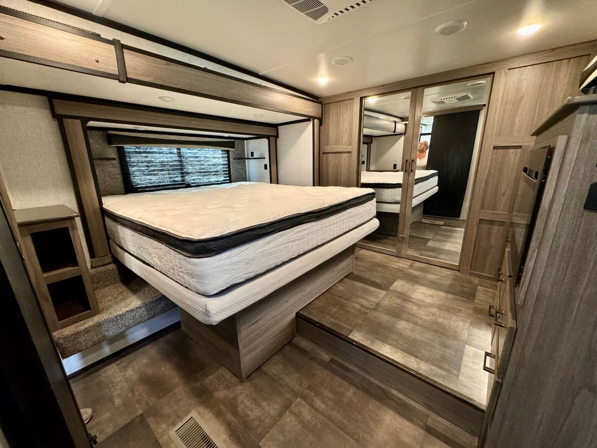 Modern RV rental bedroom with a spacious, raised bed, mirrored closet, warm wood cabinetry, and a step-up floor.. Crossroads RV Cameo 2021
