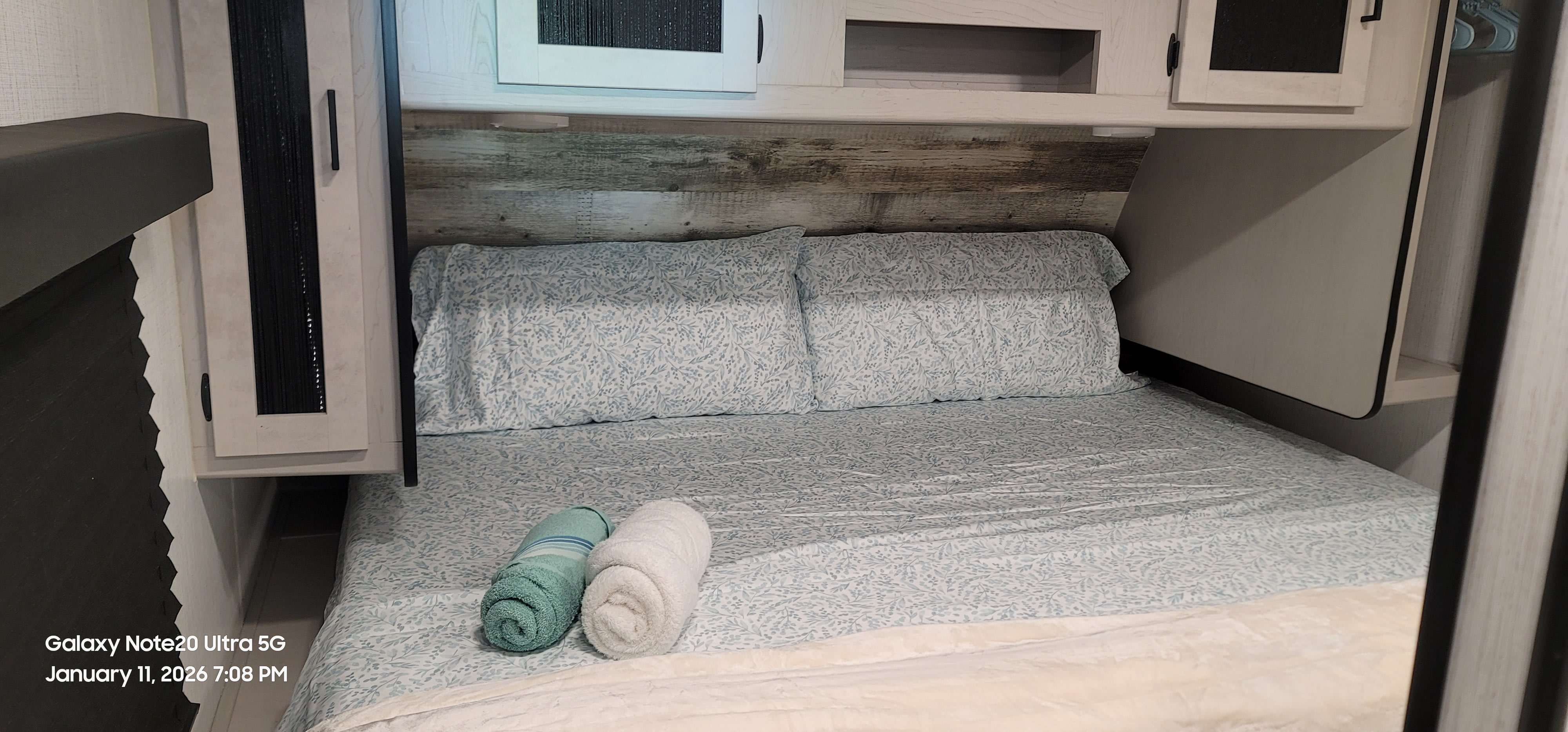 Cozy rv rental bedroom featuring a comfy bed with patterned sheets, rustic headboard, and overhead storage.. Heartland RVs Mallard 2022