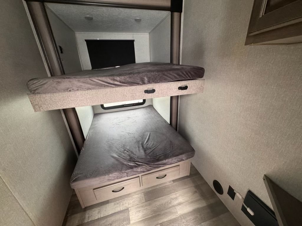 Cozy bunk beds in an RV rental, featuring grey bedding and lower bunk storage drawers. Ideal for family camping.. Forest River Coachmen Chaparral 2023