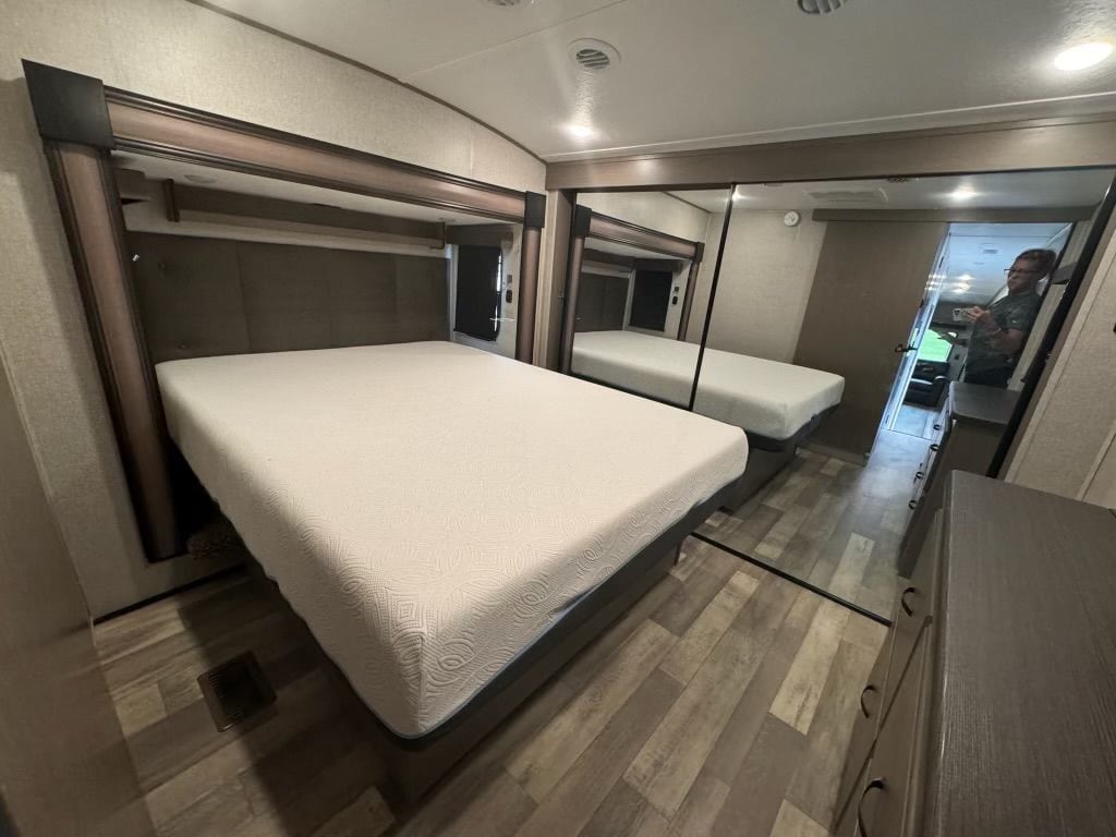 Inside an RV rental bedroom, featuring a clean bed, headboard, mirrored closet, and modern wood-look flooring.. Forest River Coachmen Chaparral 2023