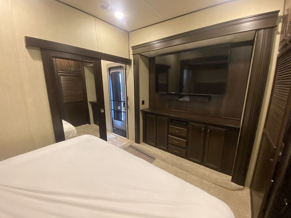 Cozy RV rental bedroom with a large bed, built-in TV entertainment center, dark wood cabinetry, and carpeted floor.. Palomino Columbus 2019