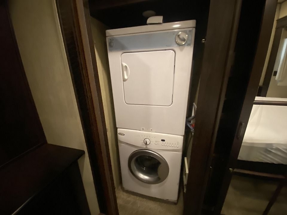Stacked washer/dryer unit in a compact RV rental, providing laundry convenience in a narrow alcove next to a sleeping area.. Palomino Columbus 2019