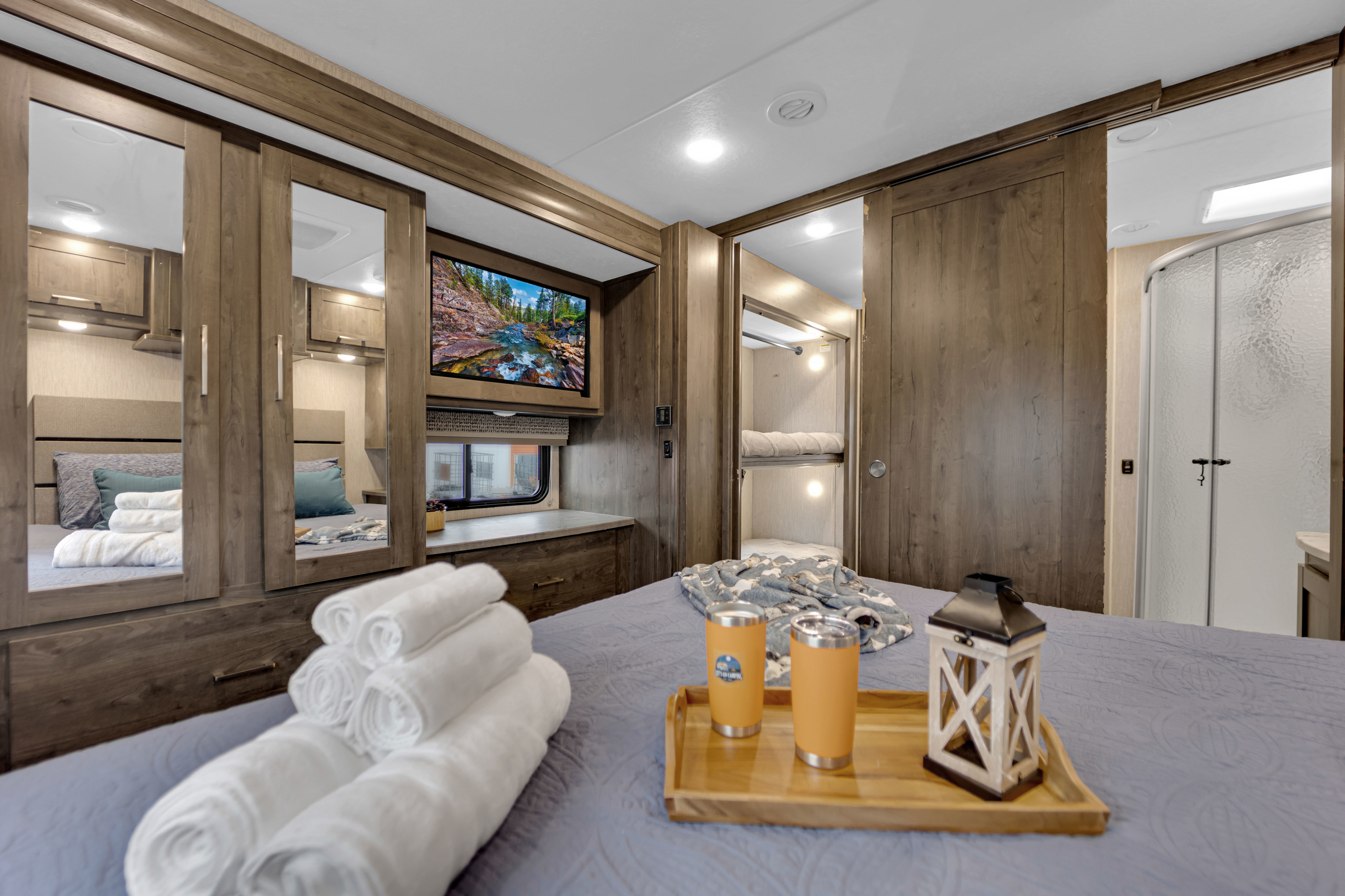 Spacious RV rental bedroom with a bed, TV, mirrored closets, bunk beds, and a private shower, perfect for travel comfort.. Coachmen Pursuit 2022