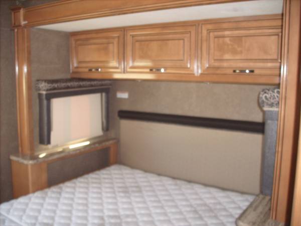 RV rental bedroom features: white mattress, light wood cabinets, and a built-in screen above a counter.. Thor Quantum 2018