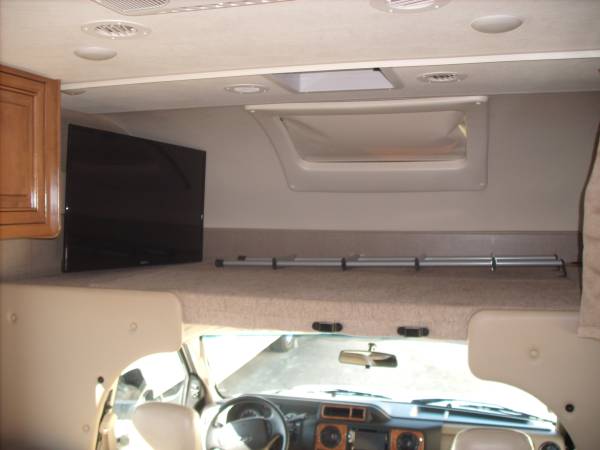 This spacious RV rental features an overhead bunk bed with safety railing, a mounted TV, and the driver's cockpit visible.. Thor Quantum 2018