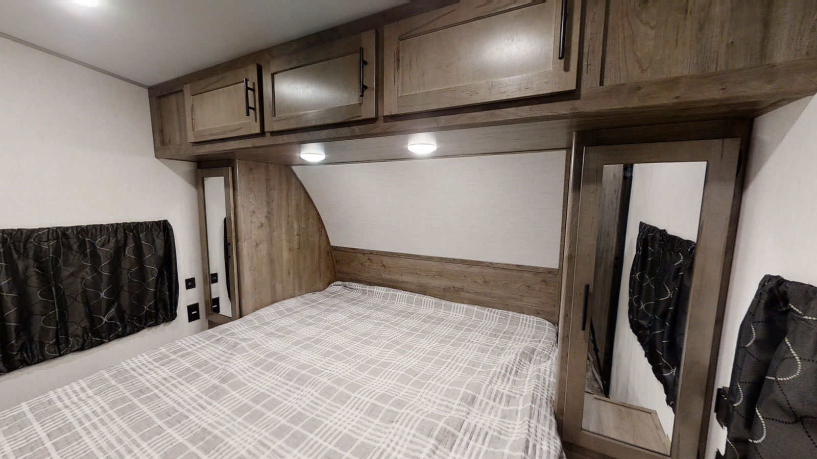 Explore this compact RV rental bedroom with a comfy bed, storage cabinets, and mirrored wardrobe doors.. Forest River Cherokee Wolf Pack 2021