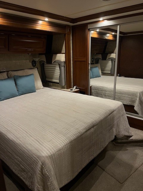 Experience comfort in this RV rental bedroom: features a cozy bed with blue pillows, wood storage, & mirrored closet.. Fleetwood Discovery 2008