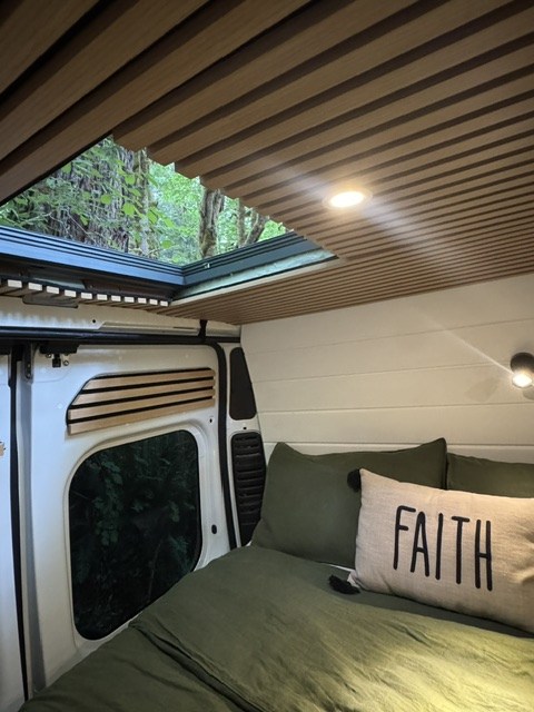Cozy RV rental interior with a comfy bed, wood-slatted ceiling, and skylight offering serene views of nature. Perfect van life!. Dodge RAM Promaster 2500 High Roof 2022