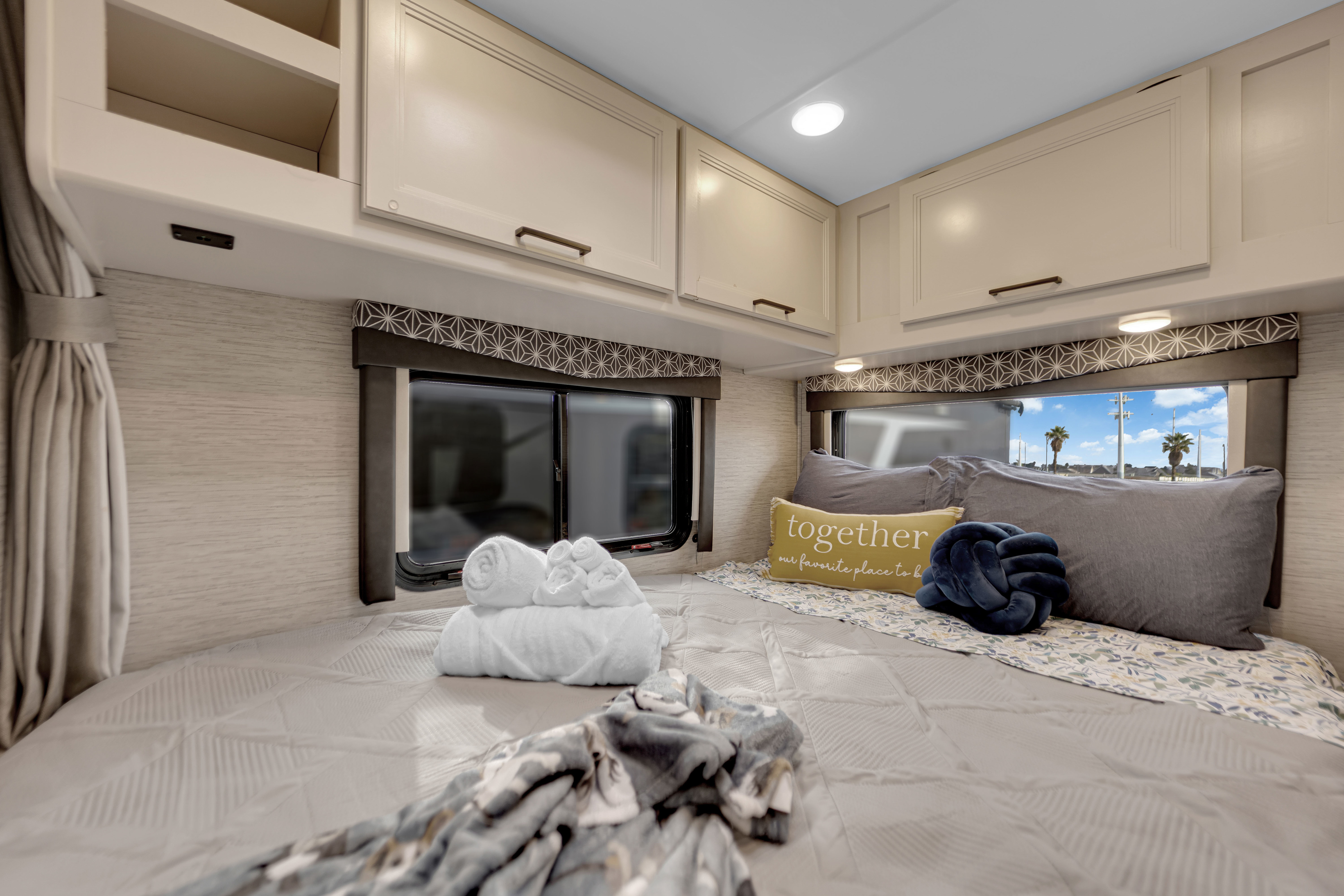 Interior of a cozy RV rental bedroom. Features a comfortable bed with soft pillows & towels, under cabinets and bright windows.. Thor Motor Coach Freedom Elite 2022