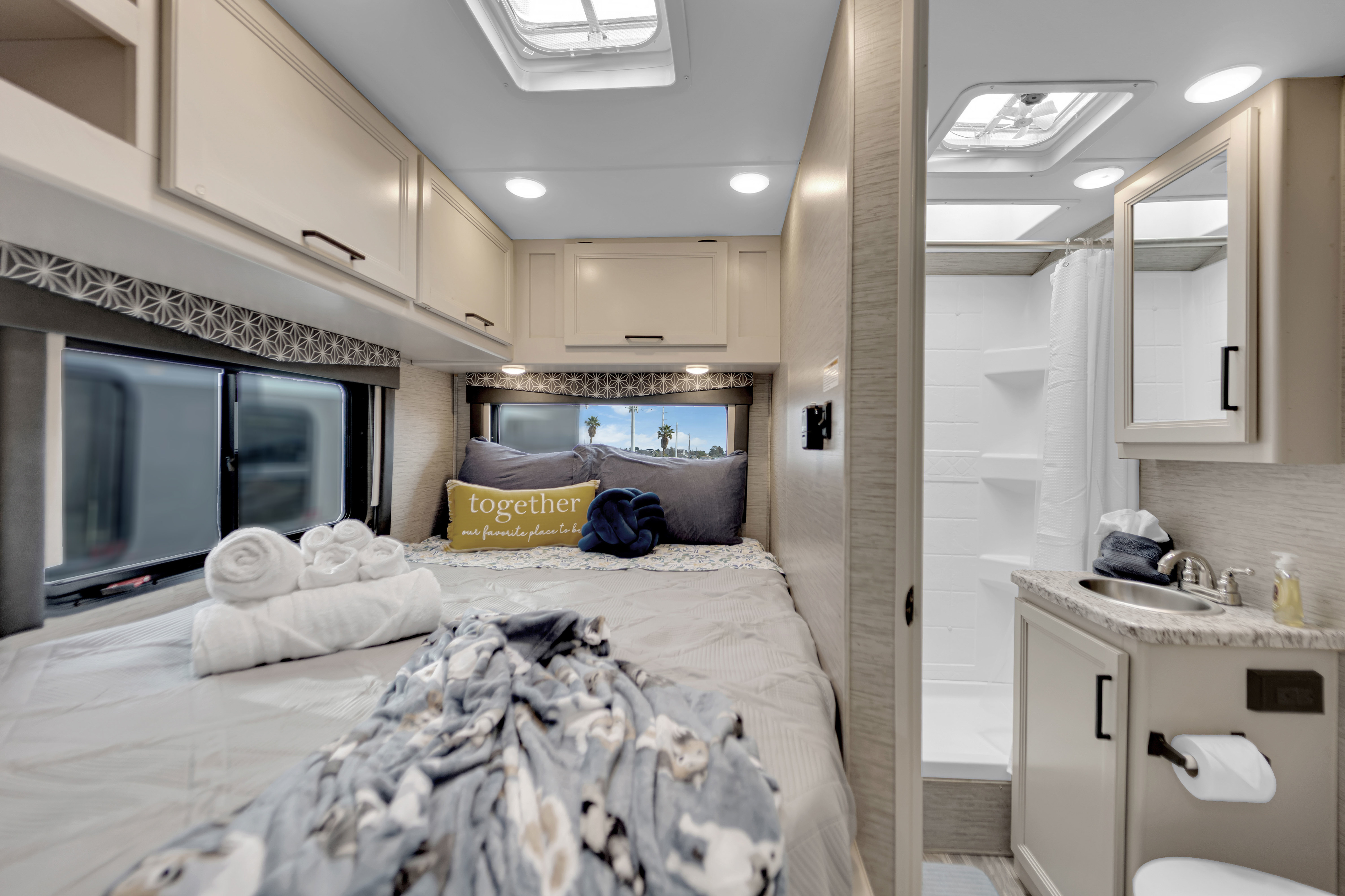 Cozy RV rental interior with a comfortable bed, overhead cabinets, and an adjacent compact bathroom with sink & shower.. Thor Motor Coach Freedom Elite 2022